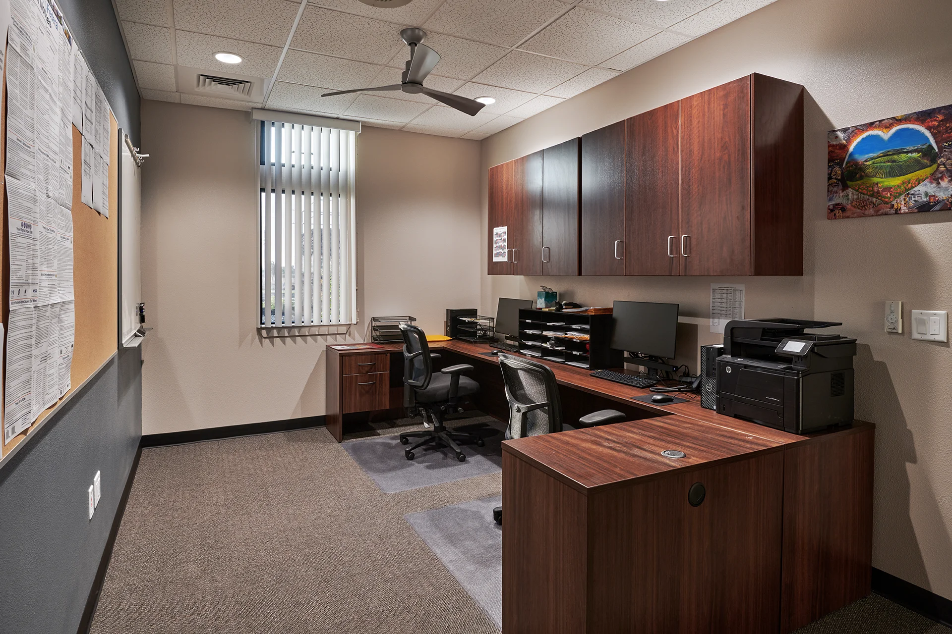 Interior office space within the civic facility showcasing a large U-shaped dark wood desk configuration, office swivel chairs, built-in storage cabinets, a wall-mounted bulletin board, and commercial carpeting.
