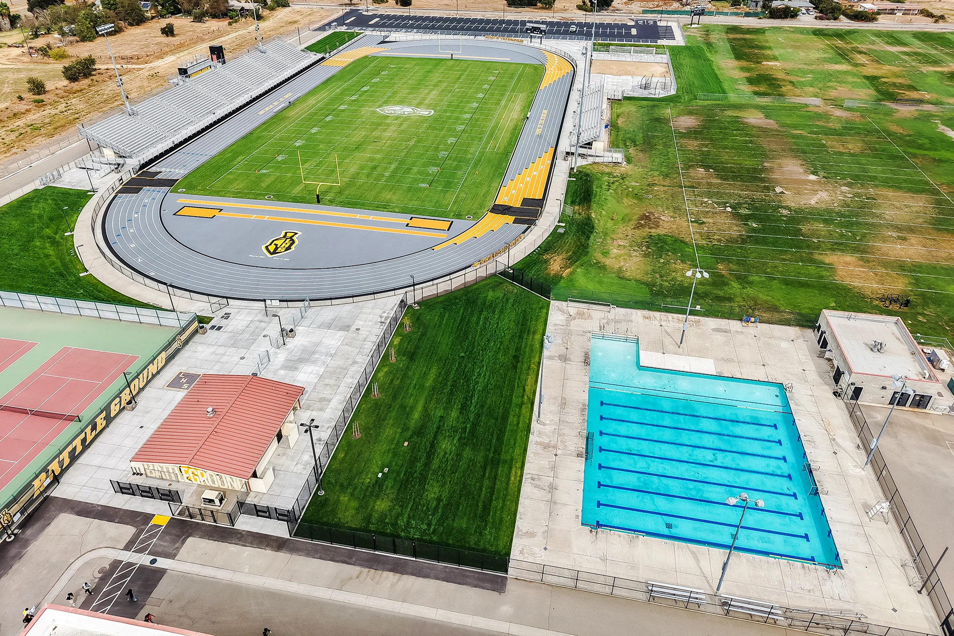 High aerial drone view of the complete Lathrop High School sports facility including stadium track, football field, and swimming pool.