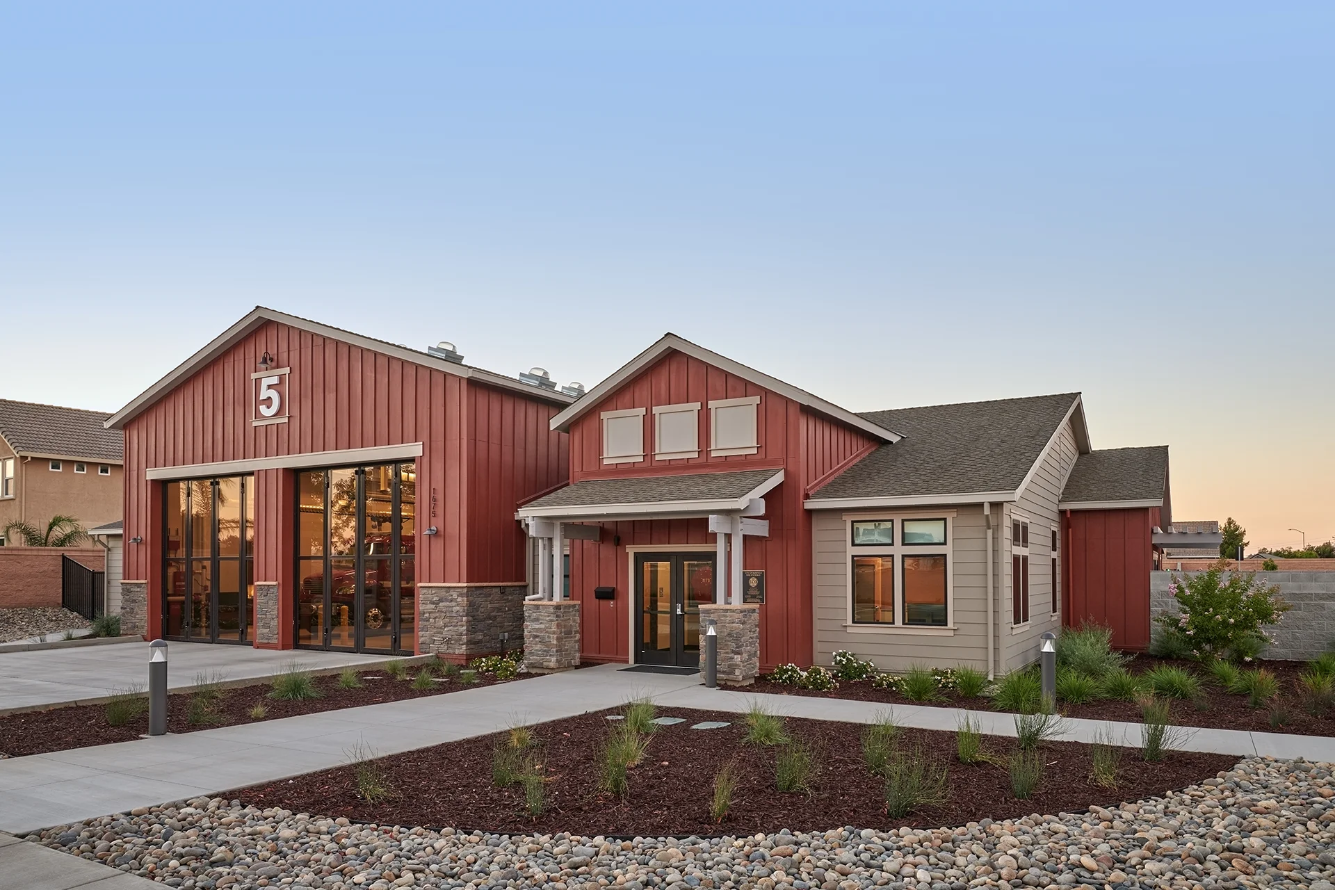 Exterior view of the municipal station building, highlighting the architectural combination of gray horizontal lap siding on the administrative offices and vertical red board and batten siding on the adjacent equipment bays.