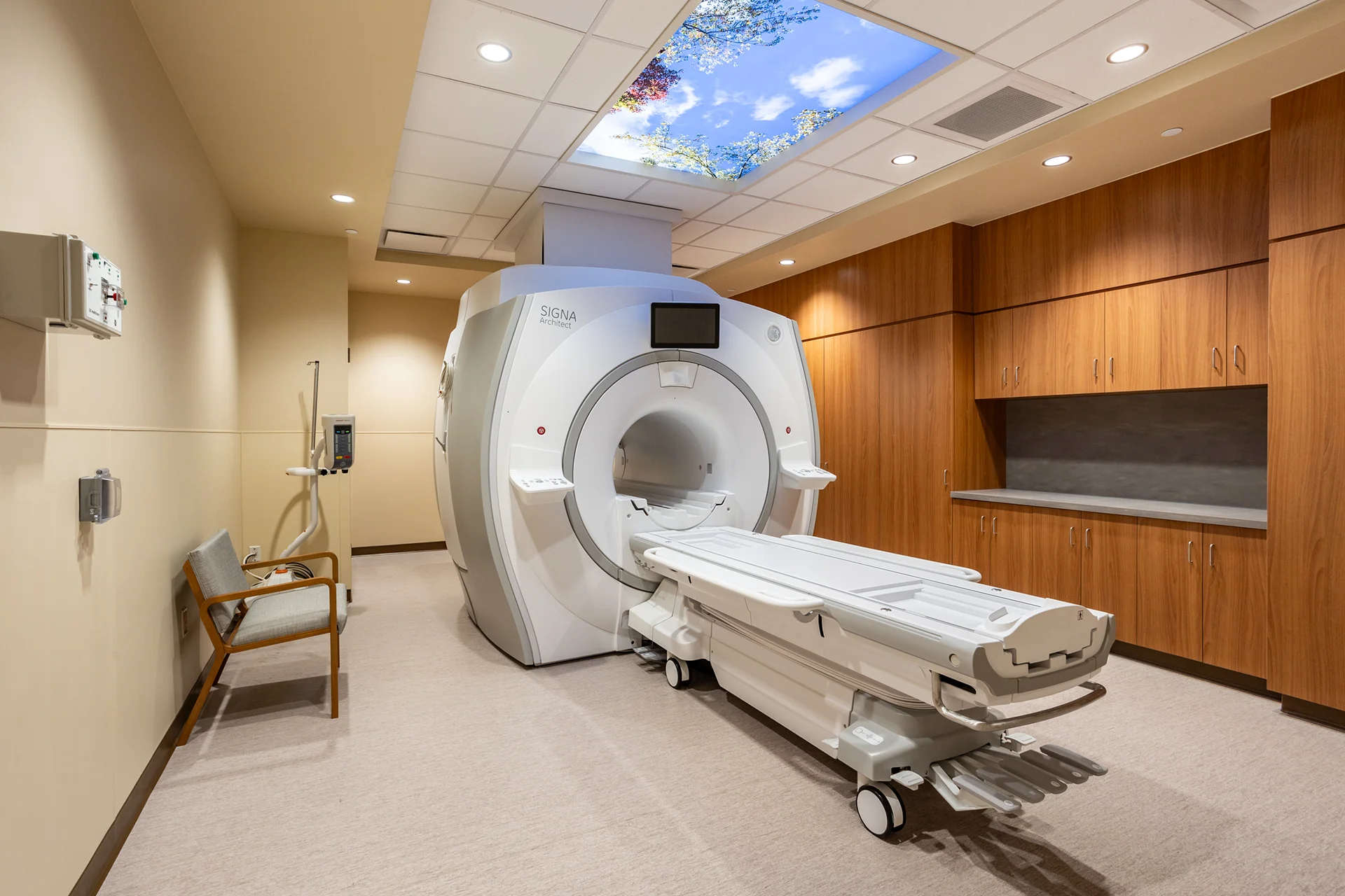 Angular perspective of a healthcare facility imaging room displaying a white multi-ton diagnostic gantry machine, an automated scanner couch, custom built-in closets, and emergency wall-mounted oxygen hookups.