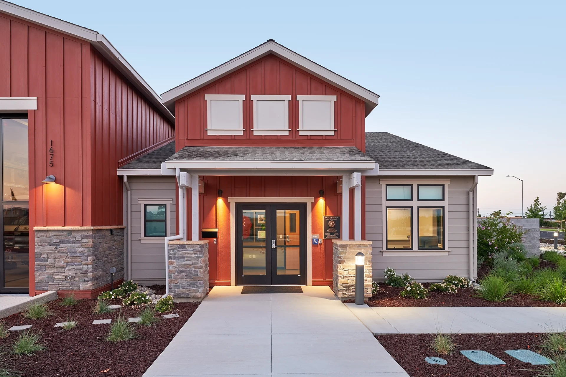 Close-up of the front entrance of the city building, showcasing double dark glass entry doors, square stone veneer base pillars, illuminated sconce lighting, and an blue ADA compliance accessibility placard.