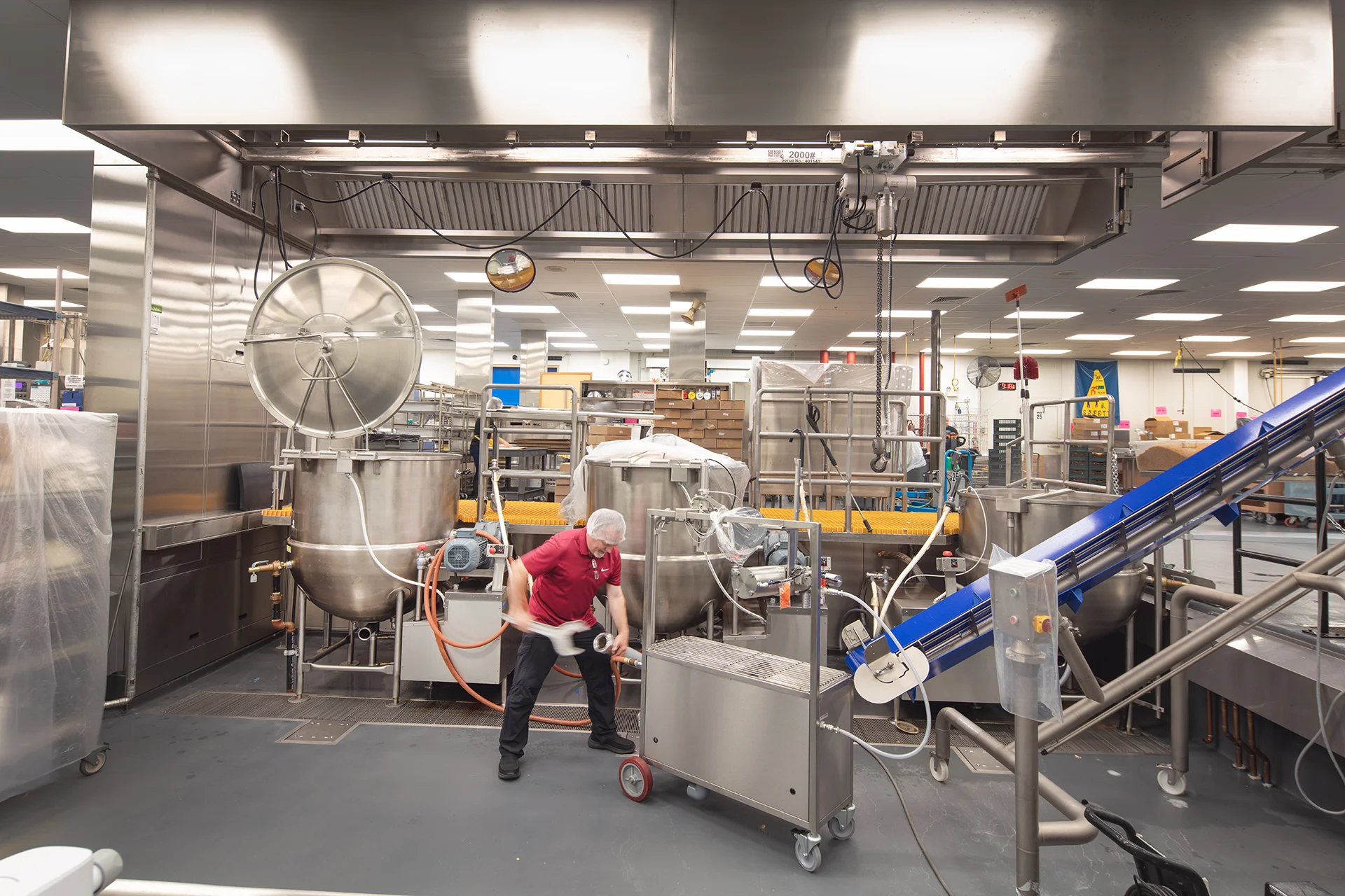 Facility installation showcase featuring a line of heavy-duty industrial mixing kettles, integrated blue belt conveyor ramps, and seamless resin commercial kitchen flooring designed for washdown maintenance.