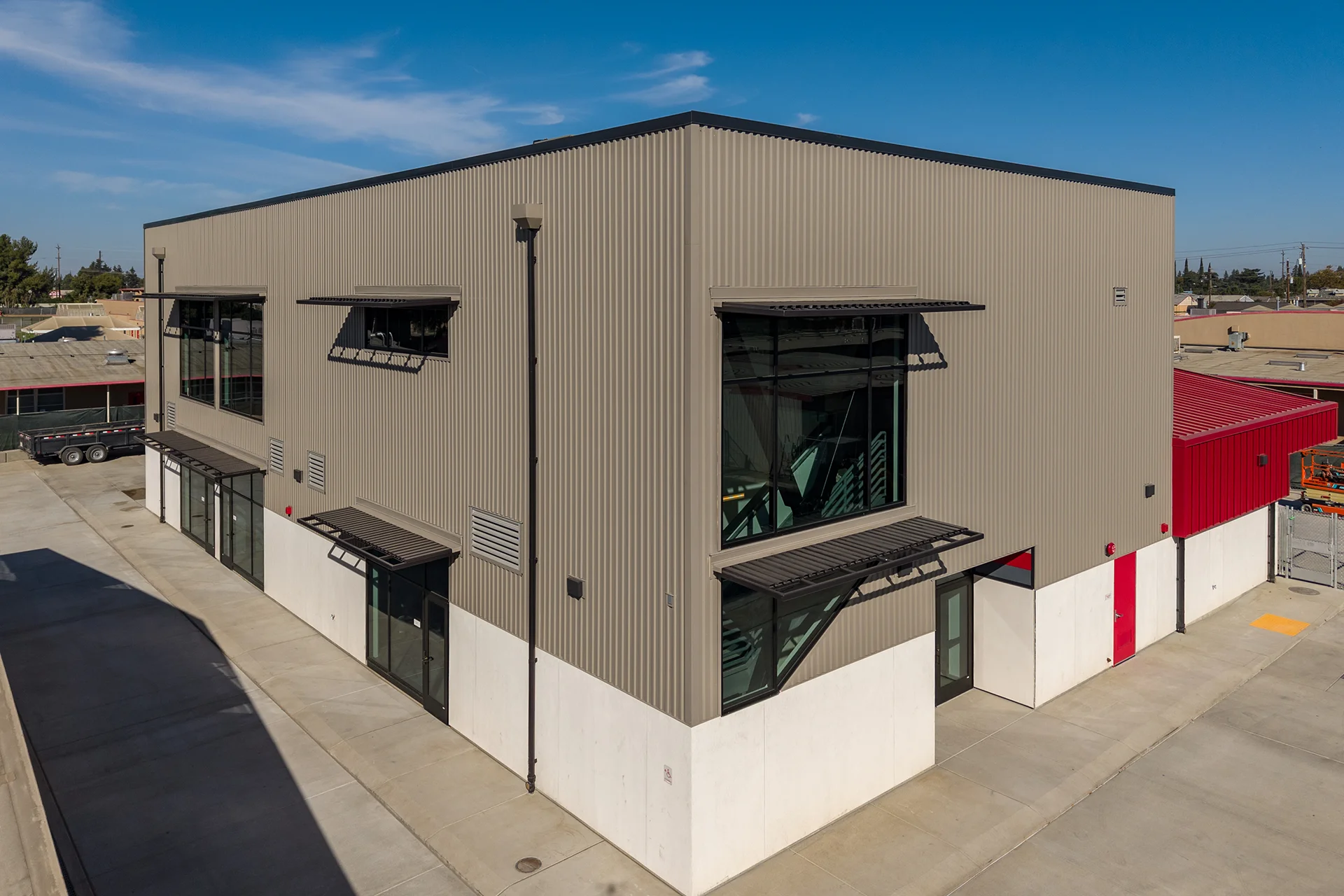 Aerial perspective of a multi-story industrial-style facility highlighting gray corrugated steel wall panels, commercial aluminum-frame windows fitted with black projecting sunshades, and a clean concrete perimeter service driveway.