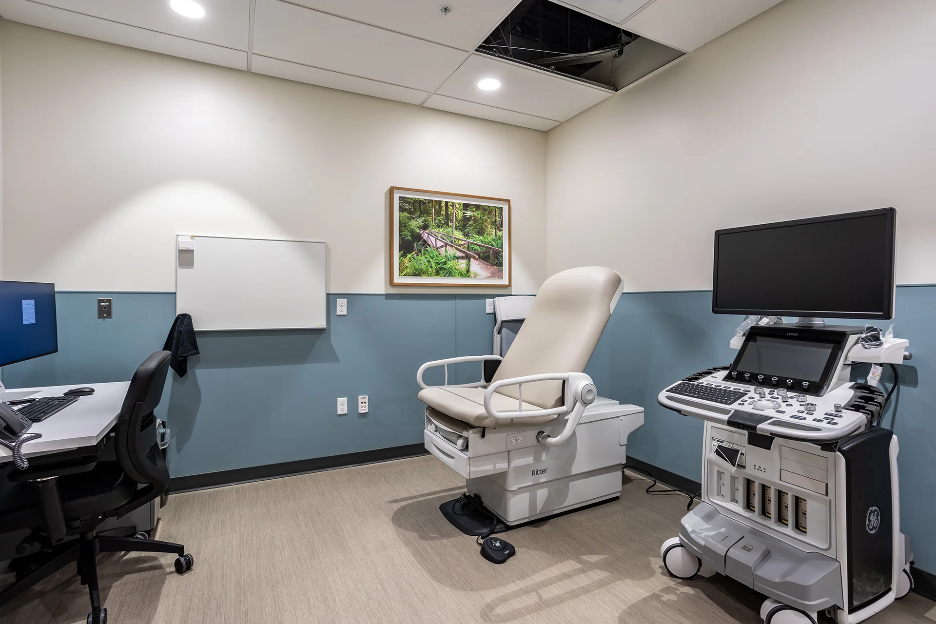 Clinical diagnostics room in San Joaquin County showcasing a GE LOGIQ ultrasound system with adjustable monitor arm, a bariatric examination table, a wall-mounted computer desk with ergonomic rolling chair, and seafoam green wall wainscoting.
