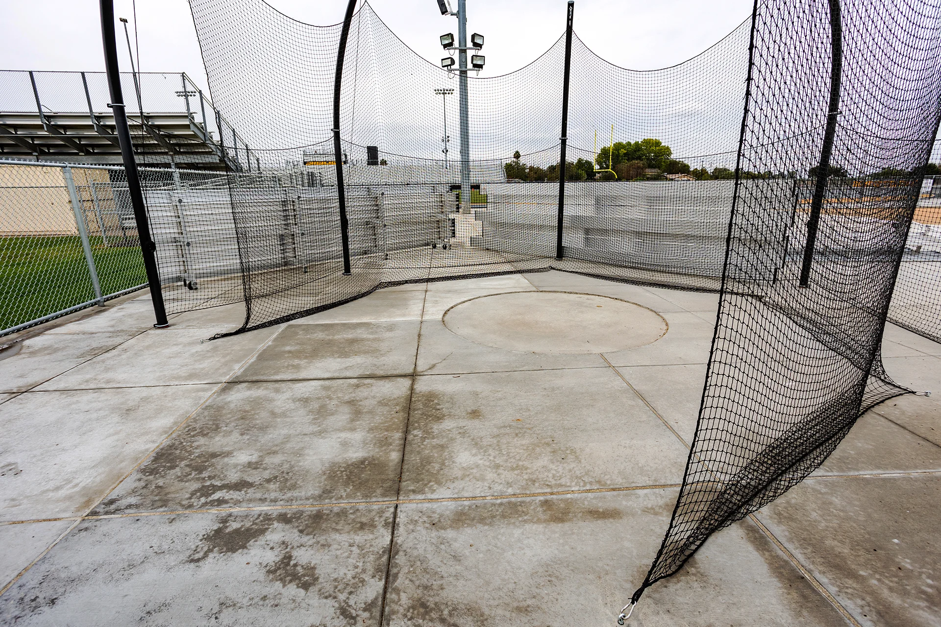 Commercial steel discus safety cage with heavy-duty black protective netting installed on a concrete pad.