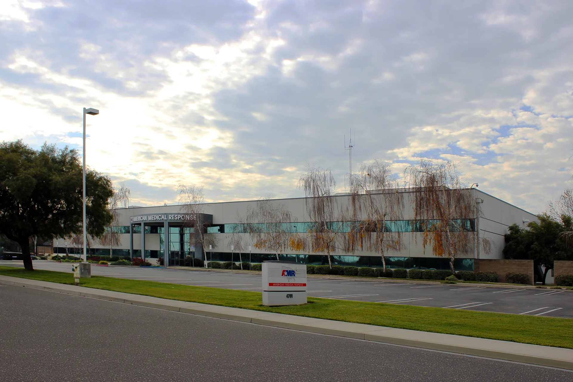 Profile view from across the street of the completed commercial office build, featuring the modern flat-roof design, integrated communication antenna tower, street lighting, and perimeter masonry walls.