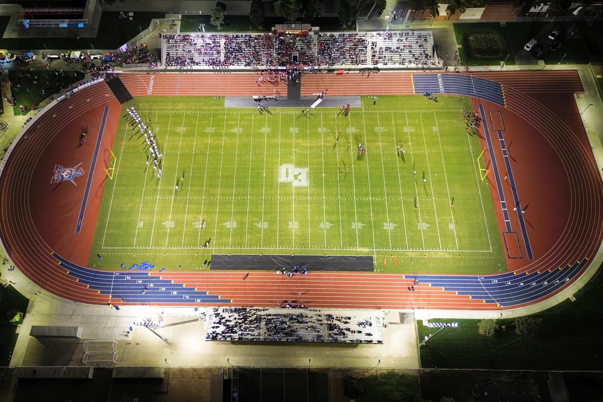 Overhead nighttime aerial view of East Union High School’s football stadium featuring an illuminated field, running track, packed bleachers, and spectators gathered for a game.