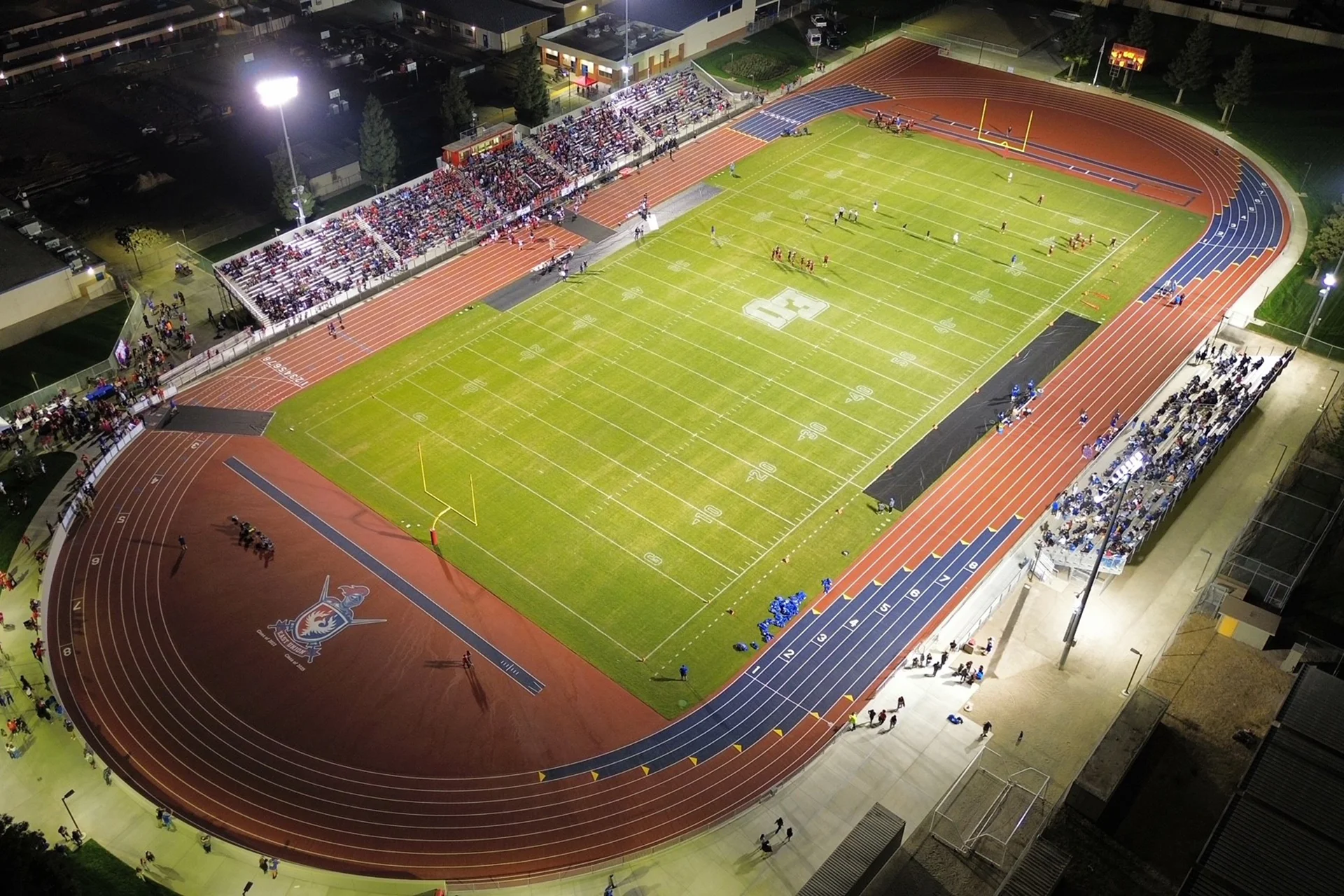 Aerial nighttime view of East Union High School’s football stadium featuring an illuminated field, running track, packed bleachers, and active game-day atmosphere.