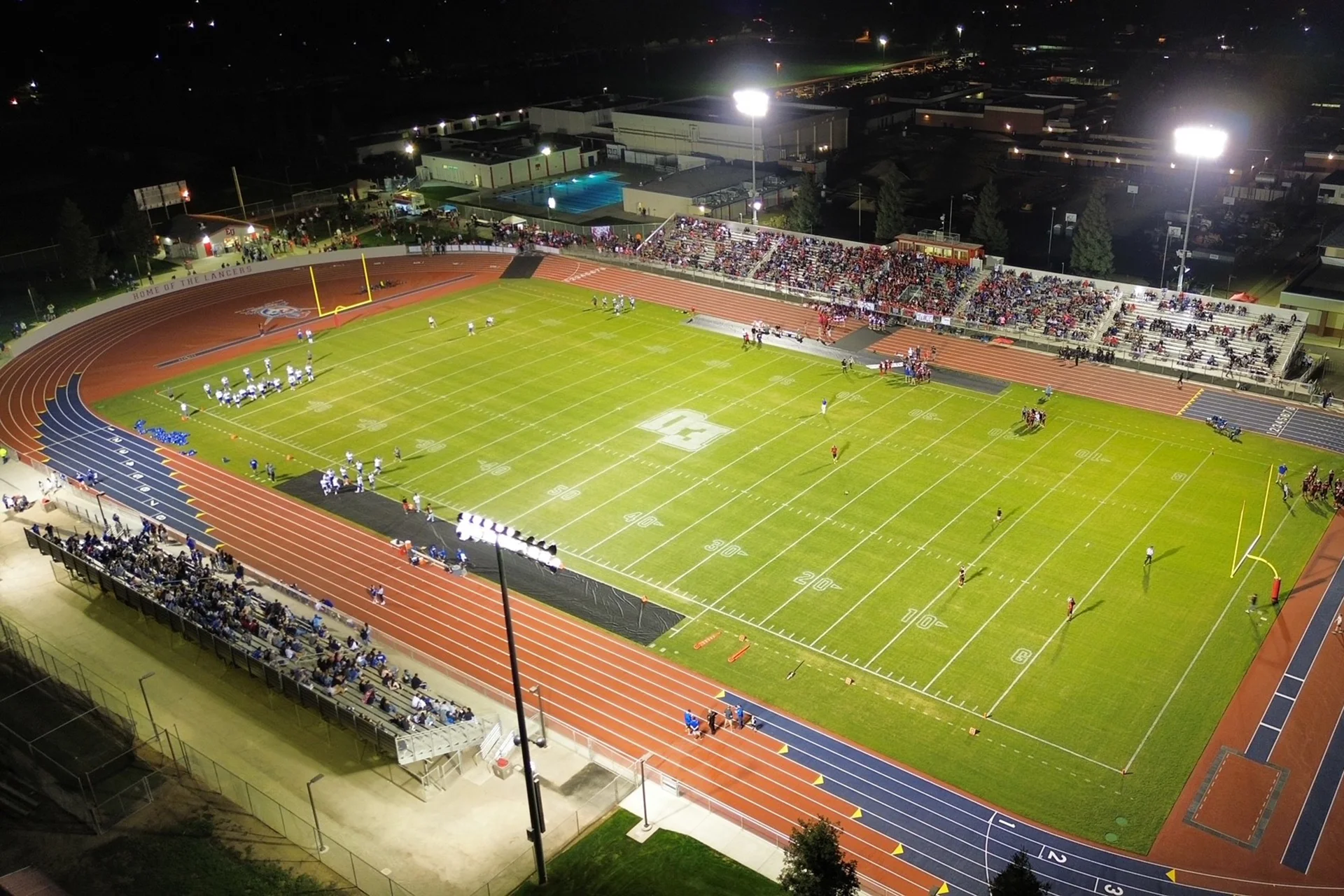 Aerial view of East Union High School’s football stadium during a nighttime game featuring a packed crowd, illuminated field, and running track.