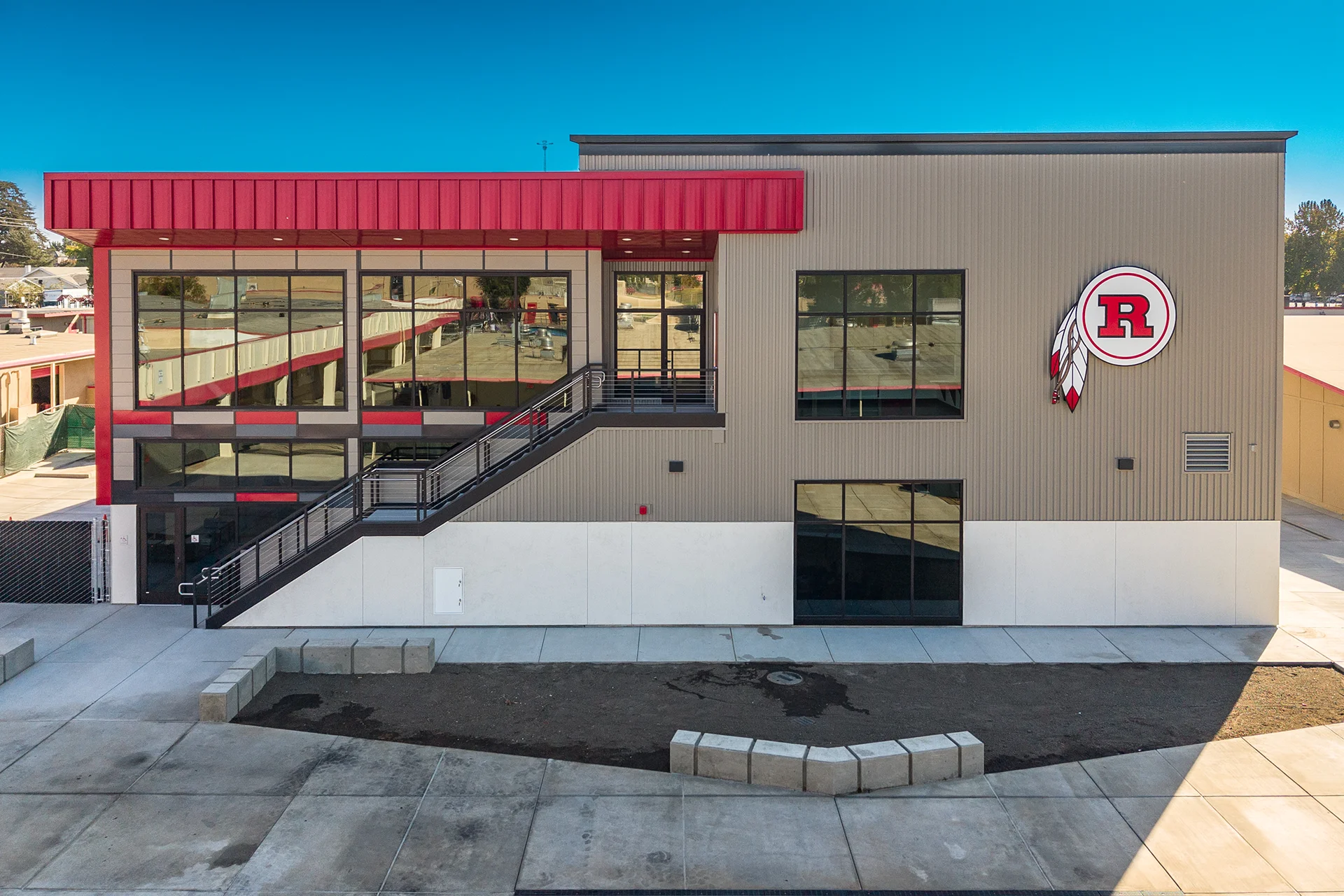 Front perspective of a modern commercial structure showcasing multi-story tinted glass curtain walls, a structural exterior steel staircase, smooth white concrete foundations, and low-maintenance architectural landscaping beds.
