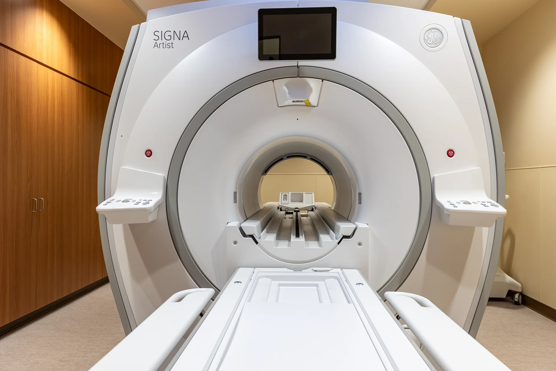 Close-up front view of a white commercial gantry system showing the circular patient aperture, technical keypad control panels on articulating mounts, and a motorized patient couch extended toward the lens.