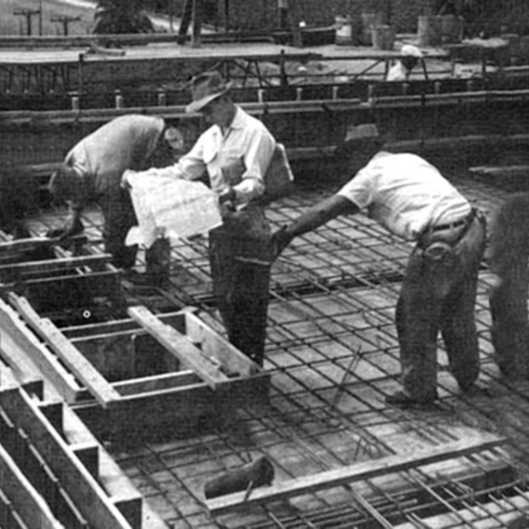 Historical Mid Century Commercial Foundation Construction Site Historic black-and-white photograph from the mid-1940s showing a construction crew in Escalon, California, reviewing architectural blueprints over an expanse of steel rebar reinforcement grid matrix prior to a concrete pour.