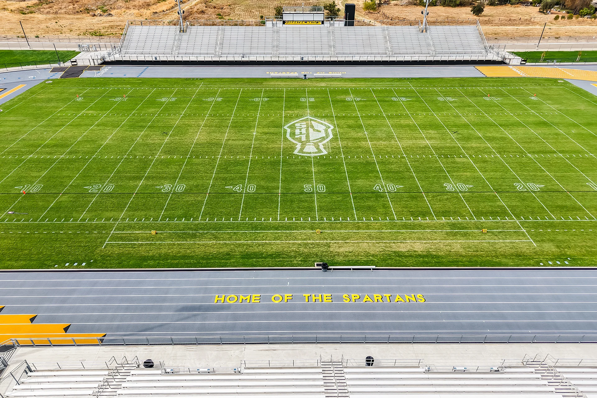 A top-down aerial shot of the 50-yard line with a large white Lathrop High School logo, and the yellow text 