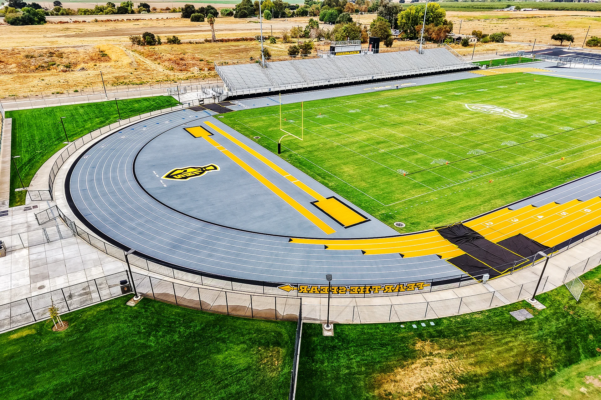 A top-down aerial photograph looking over the entire Lathrop High School stadium, featuring green grass, a grey track, and a vast landscape beyond.