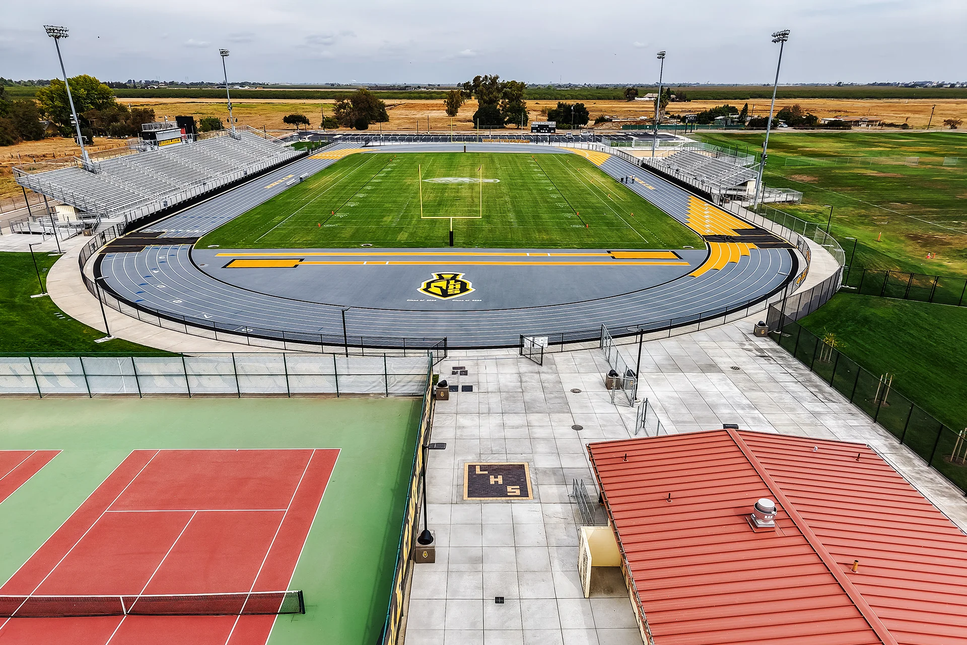 Aerial view of a synthetic running track surrounding a green football field with bleachers at Lathrop High School stadium.