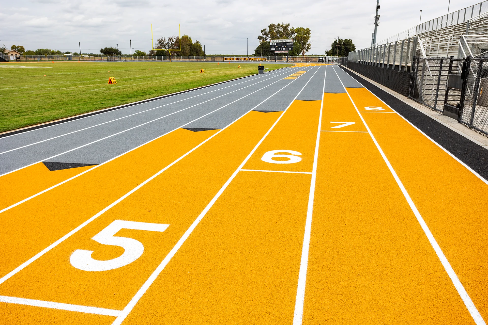 Lathrop High School running track with numbered sprint lanes, football field, scoreboard, goalposts, and stadium bleachers in the background.