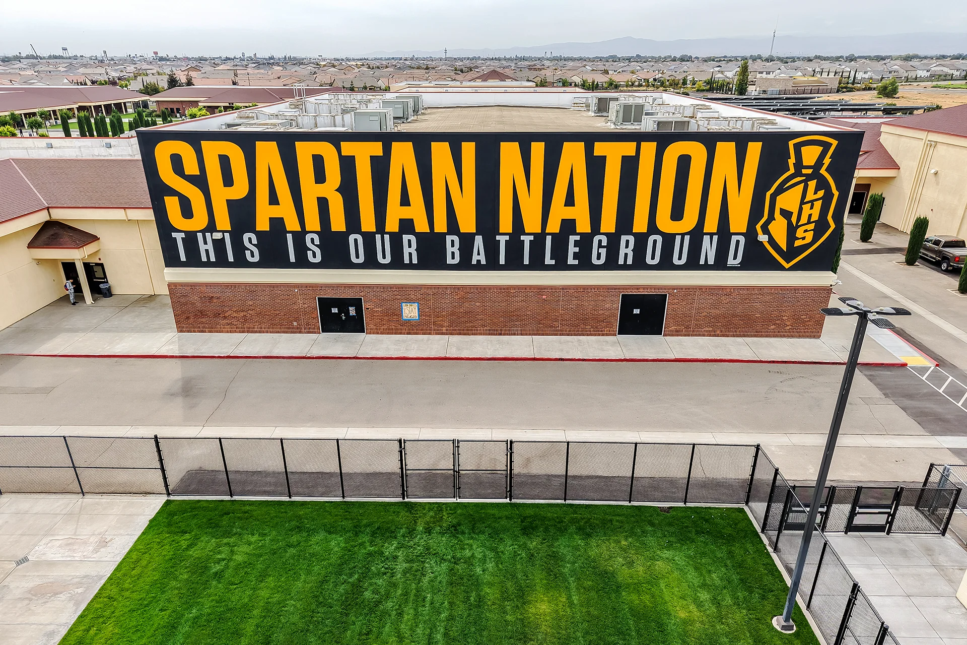 Aerial view of a brick school building featuring a large black and yellow Spartan Nation mural next to a concrete walkway.