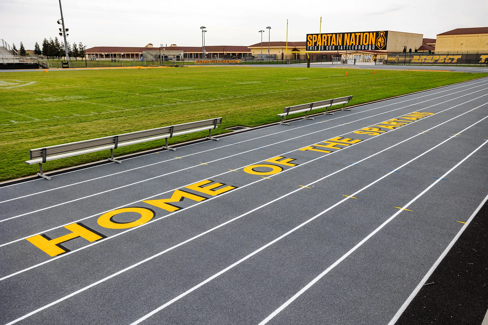 Lathrop High School running track featuring Home of the Spartans branding alongside the football field, benches, and Spartan Nation stadium signage.