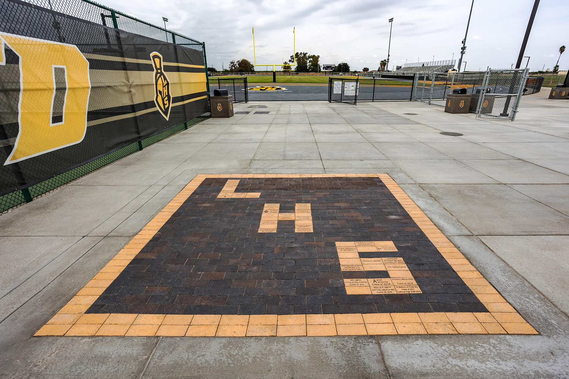 Donor recognition brick plaza at the entrance to Lathrop High School’s stadium with the athletic field, track, and goalposts visible beyond.