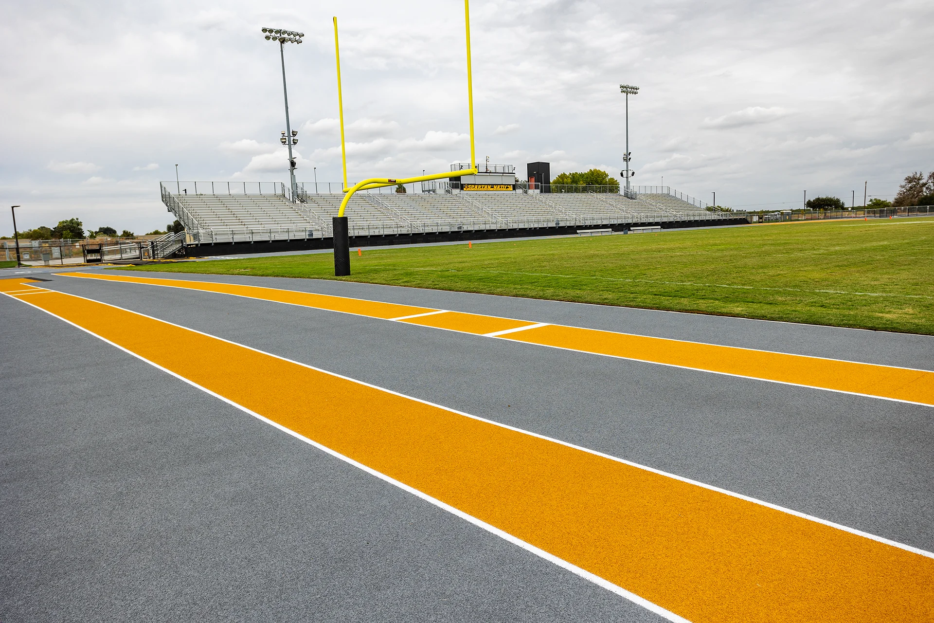 Lathrop High School football field end zone with goalposts, stadium bleachers, and track surface featuring black and gold school colors.
