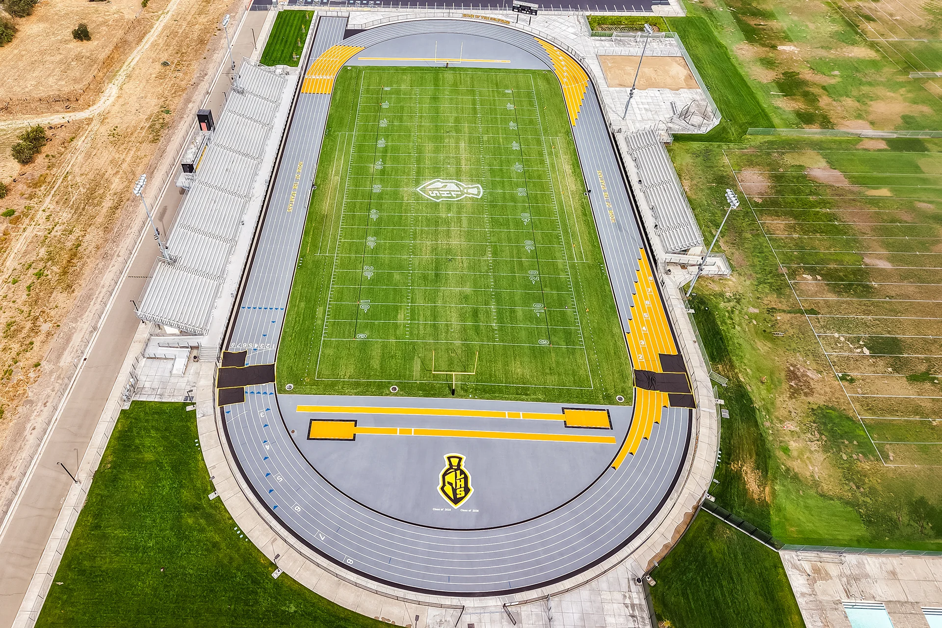 High aerial drone view of the complete Lathrop High School sports facility including stadium track, football field, and swimming pool.