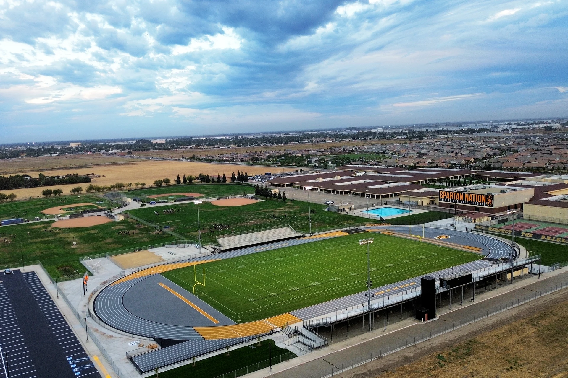 Aerial view of Lathrop High School’s football stadium, running track, athletic fields, aquatics center, and surrounding campus under a dramatic cloudy sky.