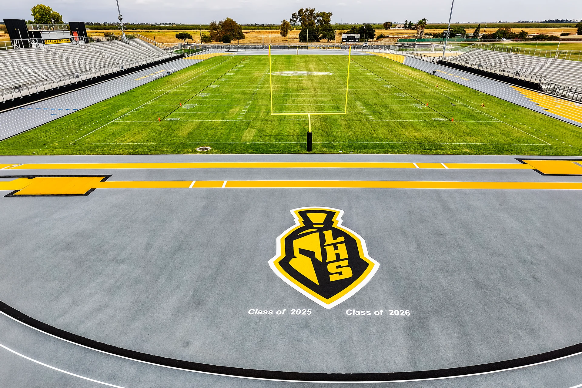 A close-up aerial photograph of a grey track curve with vibrant yellow markings and a large yellow and black Spartan head logo.