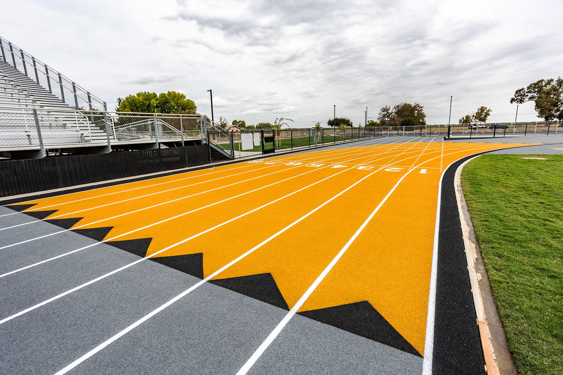 Lathrop High School running track featuring numbered sprint lanes, black and gold lane markings, and stadium bleachers alongside the football field.