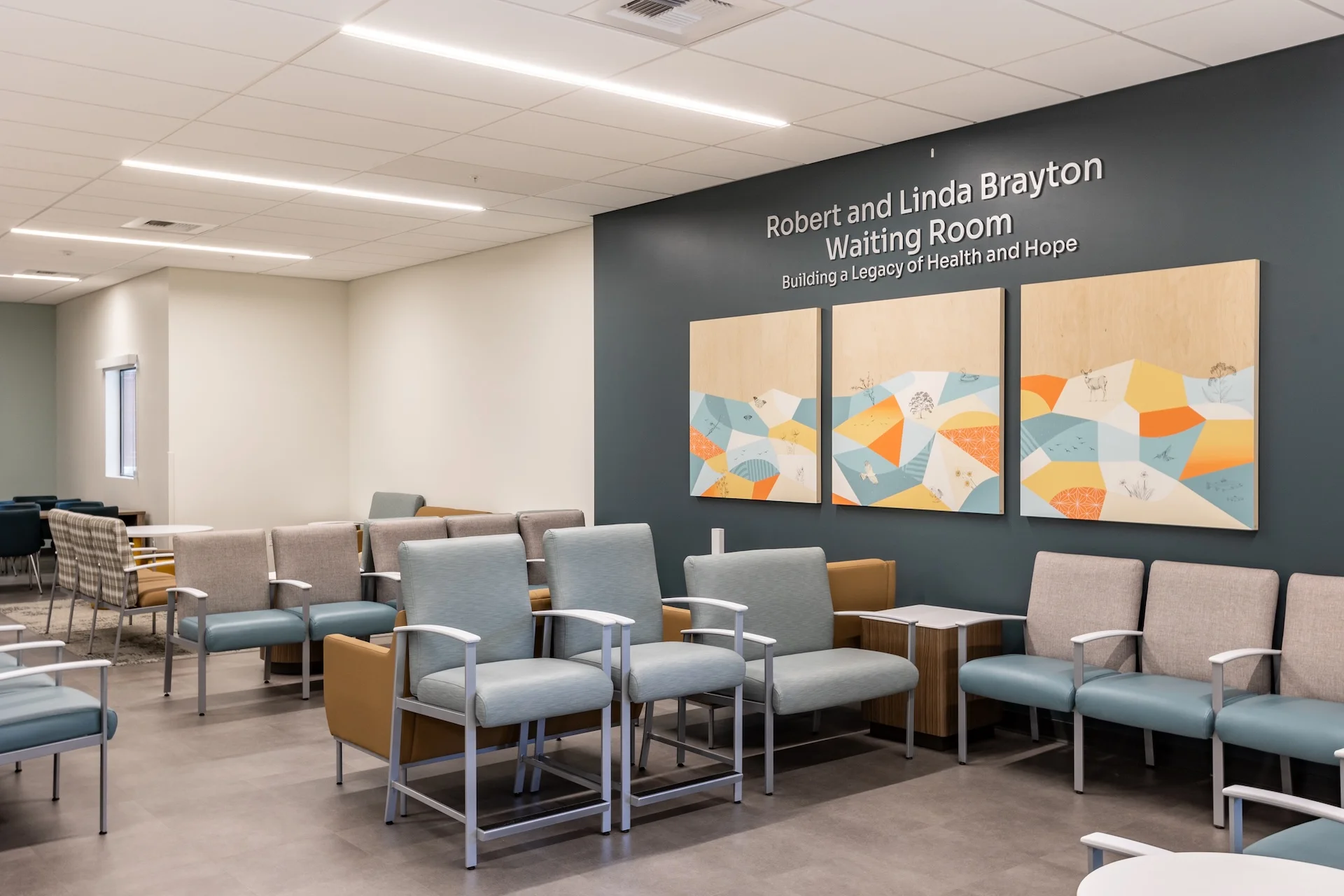 Angular view across a medical facility waiting room highlighting high-traffic commercial carpeting in the background, a central arrangement of steel-frame medical armchairs, neutral wall treatments, and architectural linear slot diffuser grilles integrated into a white acoustic ceiling.