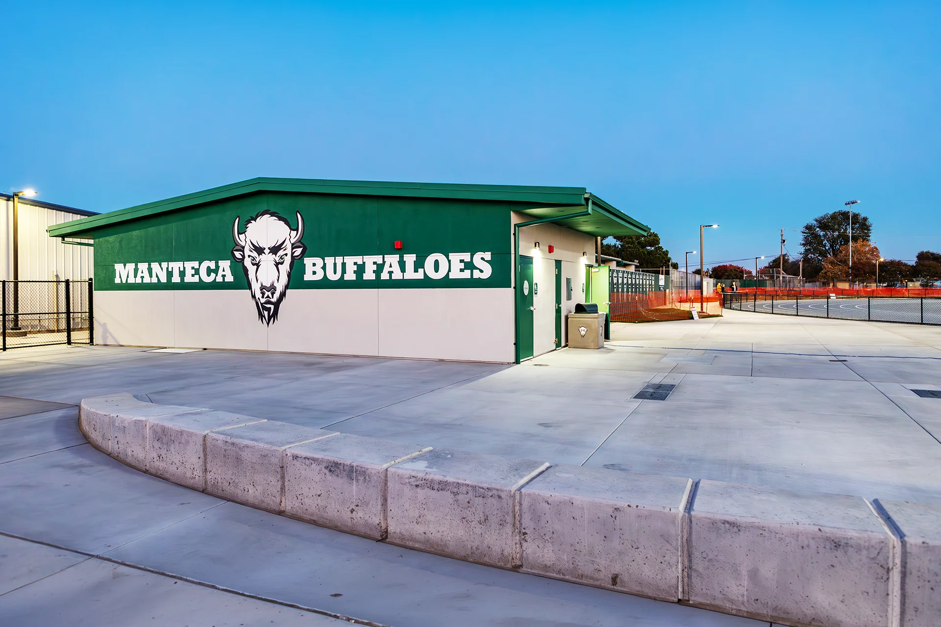 Exterior view of Manteca High School athletic facilities featuring Buffaloes branding beside the renovated track complex at dusk.