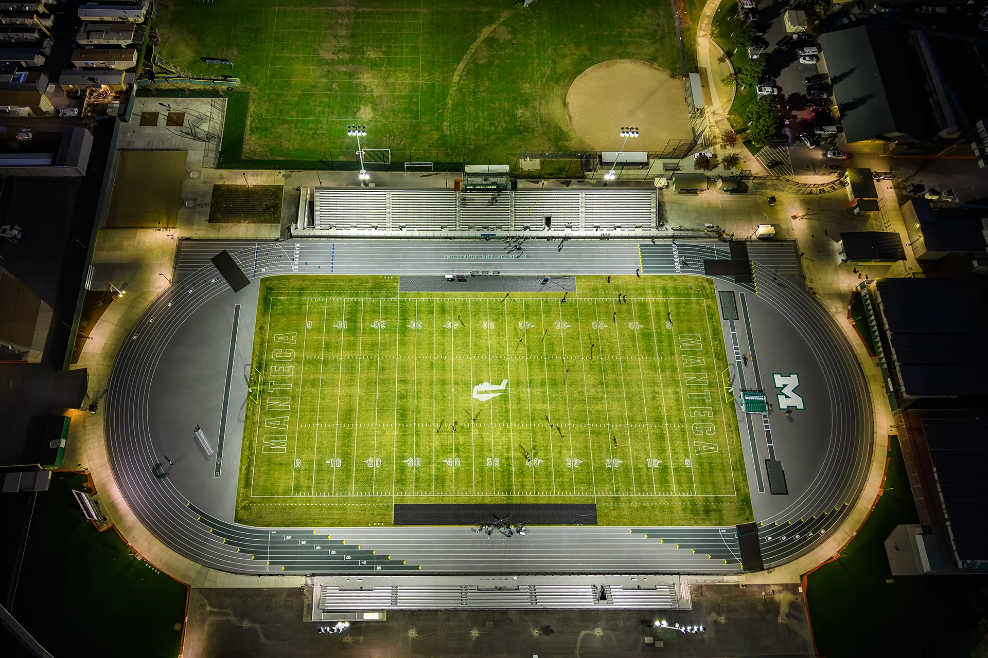 Top-down aerial view of Manteca High School’s illuminated football stadium, running track, and bleachers at night following the renovation project.