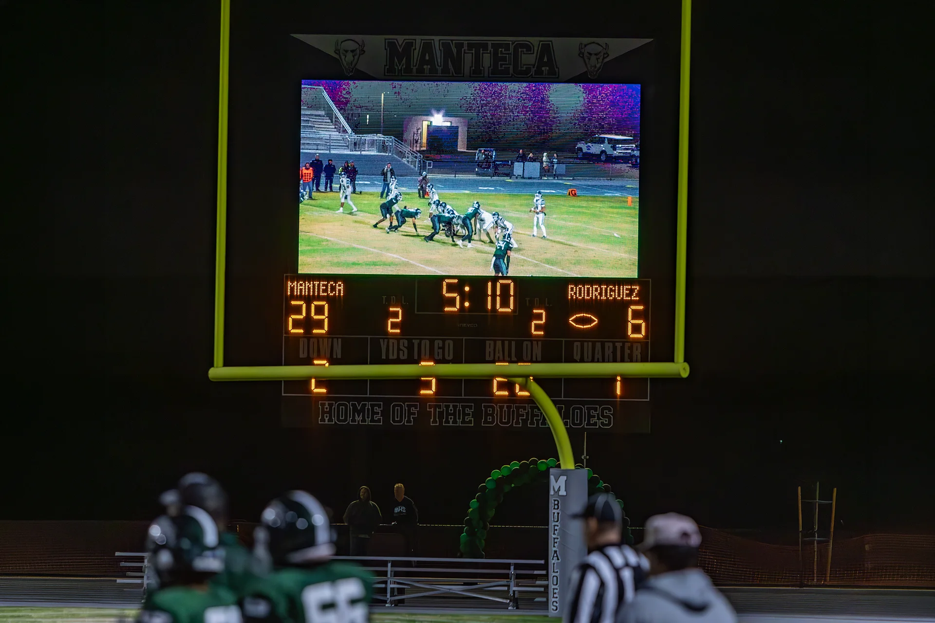 Digital video scoreboard displays live football game action at Manteca High School during a nighttime game under the stadium lights.