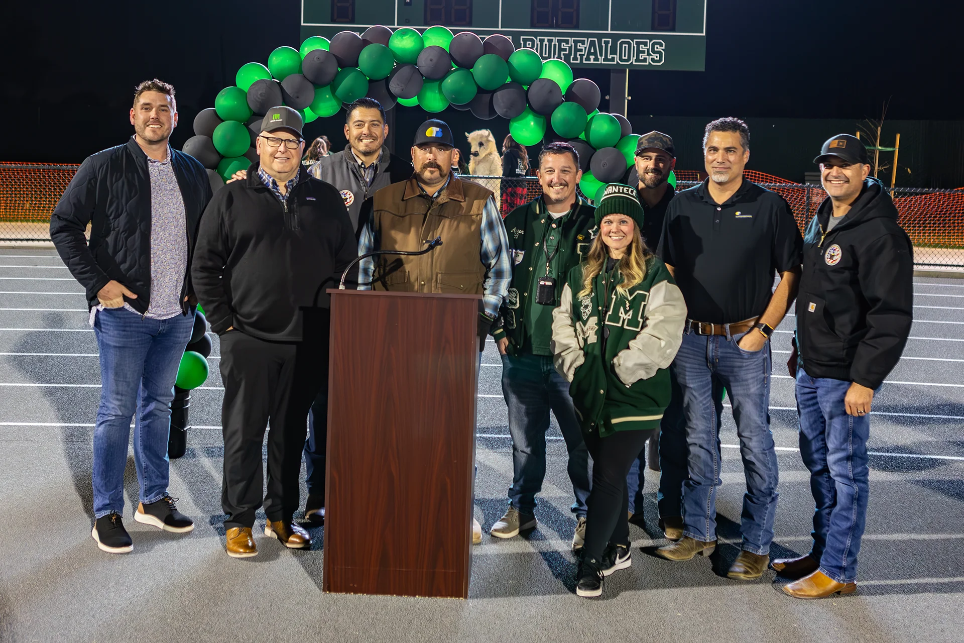 Project partners and community members pose beneath a green and black balloon arch during the Manteca High School track renovation celebration.