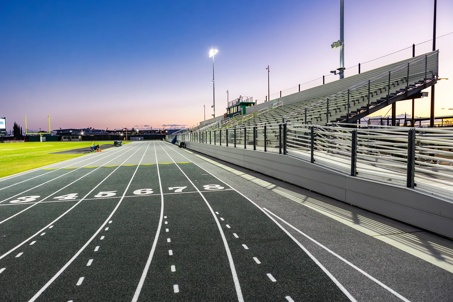 Running track and stadium bleachers at Manteca High School illuminated under stadium lights at sunset.