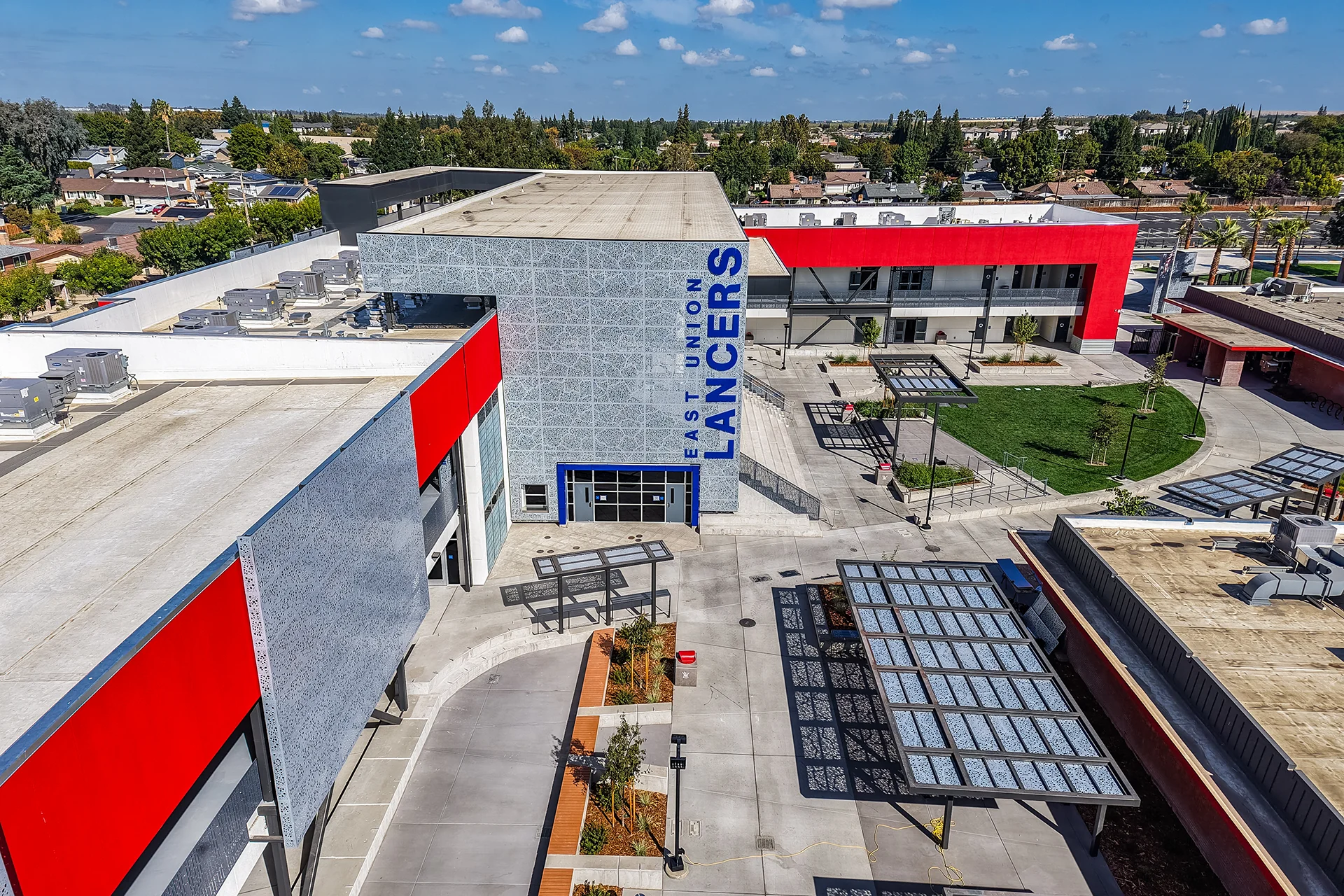 Wide drone survey of a high school facility layout in Manteca, California highlighting freshly installed flat commercial roofing membranes, roof-mounted HVAC systems, a central green courtyard, and integrated steel awnings.