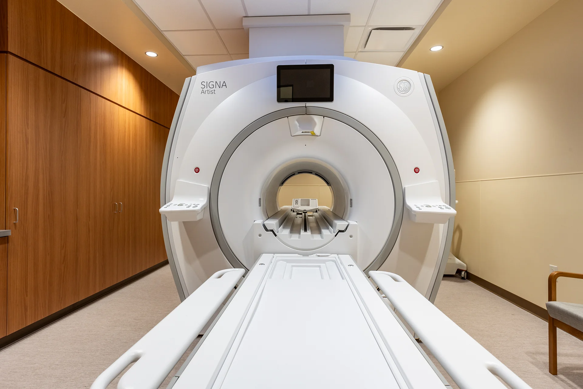 Direct front-on perspective looking through the open patient bore of a commercial medical scanner system, showing the integrated track bed, adjustable head coil cradles, and flush wood-grain cabinetry accents.