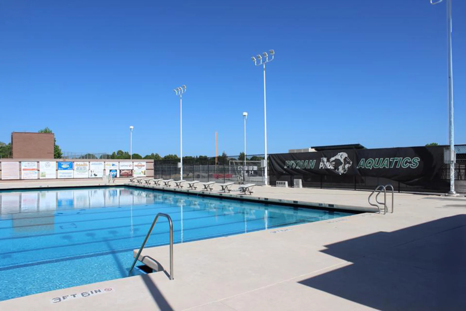Outdoor competition pool at Pitman High School featuring swim lanes, deck access points, and aquatics branding along the perimeter fence.