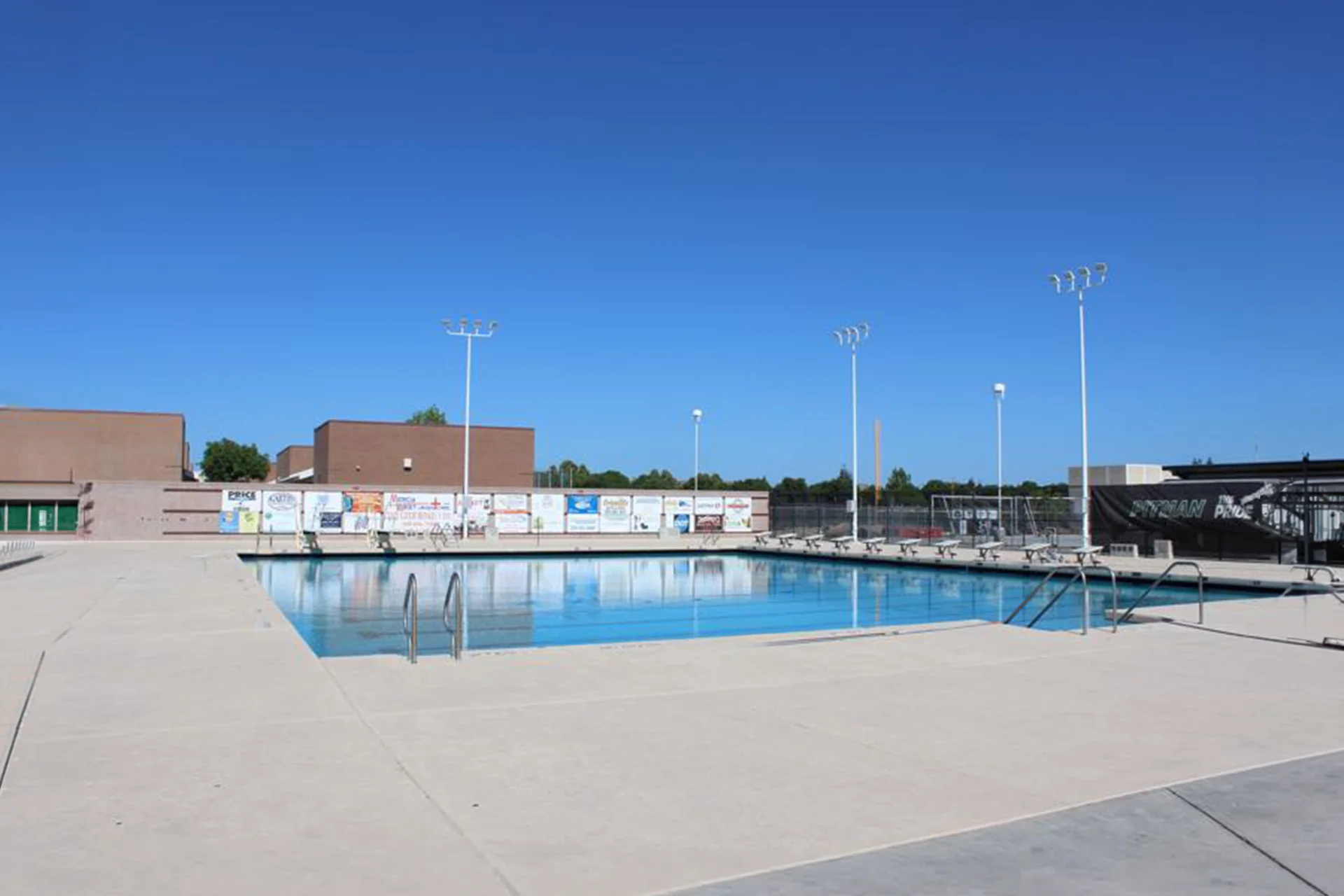 Outdoor swimming pool and surrounding deck area at Pitman High School’s aquatics facility under a clear blue sky.
