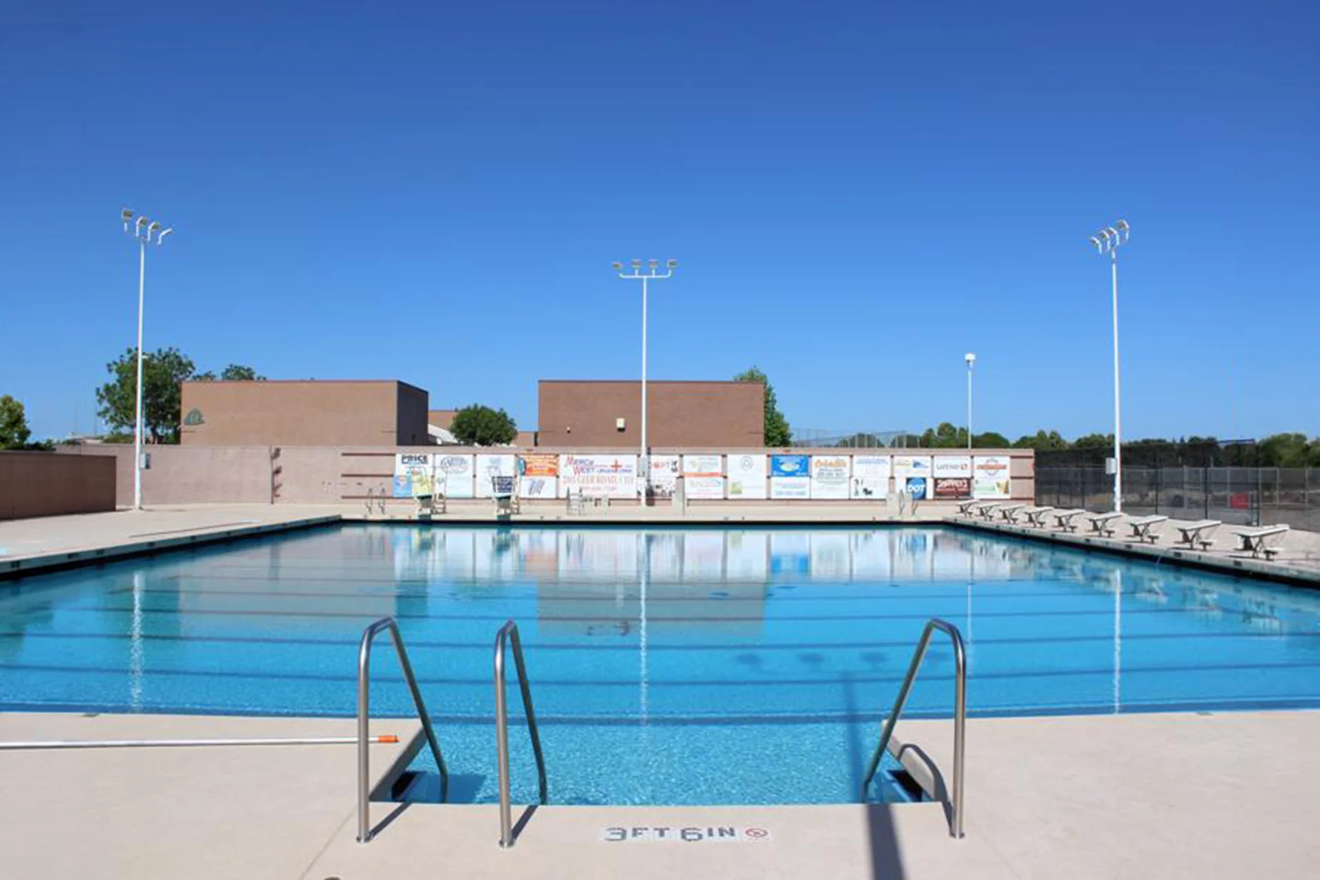 Competition swimming pool at Pitman High School featuring lap lanes, entry handrails, and a spacious pool deck under a clear sky.