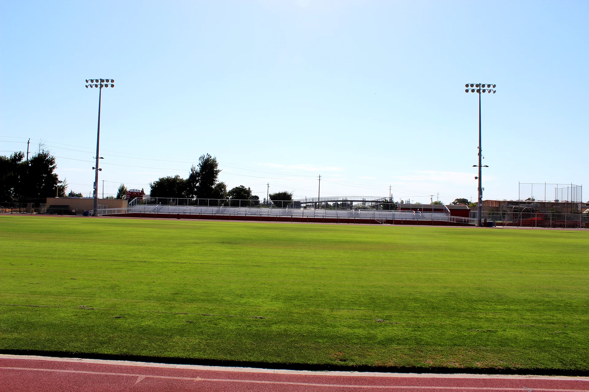 Wide view of Ripon High School’s football field, running track, stadium bleachers, and field lighting under a clear blue sky.