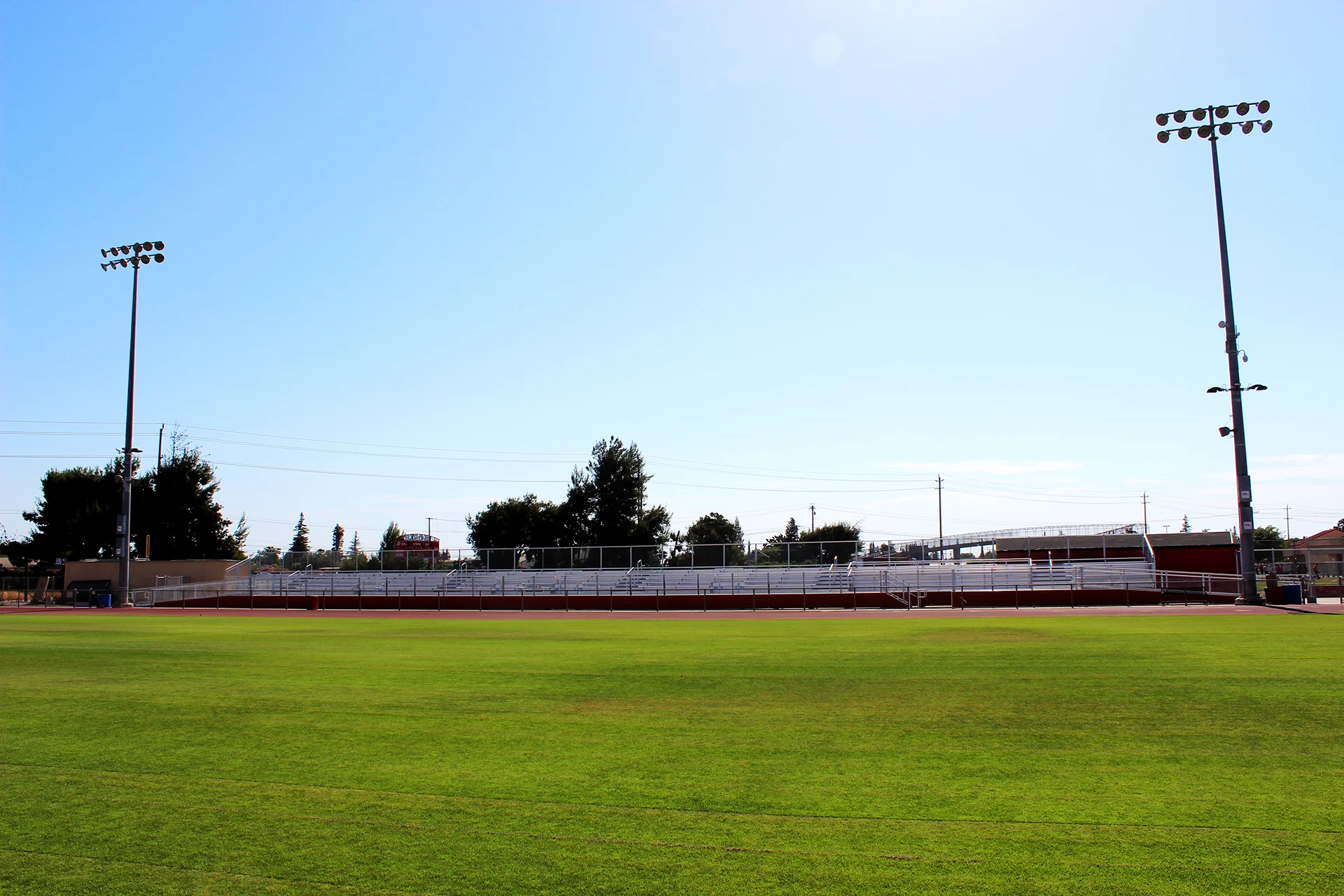 Ripon High School athletic field with stadium bleachers and field lighting towers visible beyond the grass playing surface on a clear day.