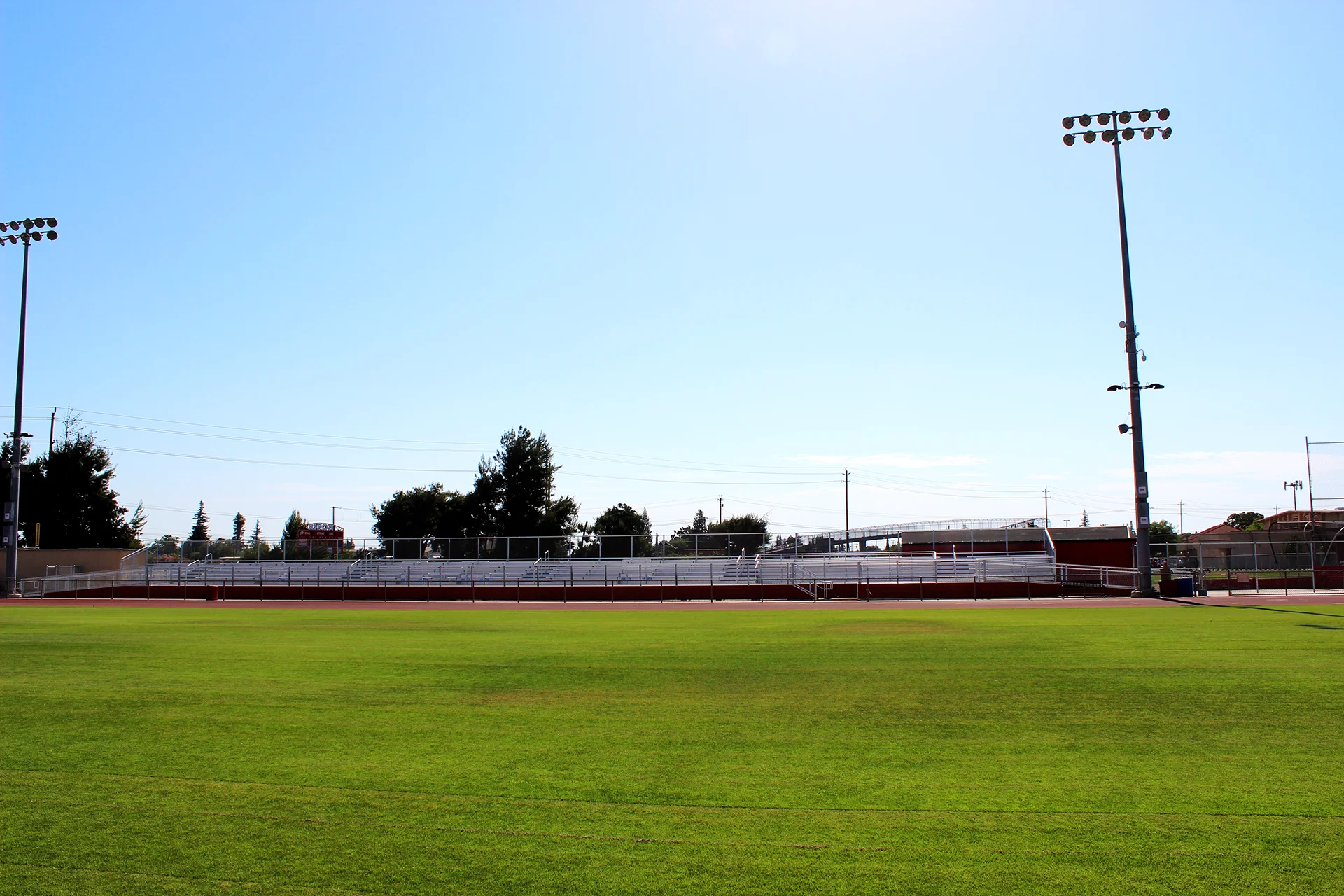 Ripon High School athletic field with stadium bleachers and field lighting visible beyond the grass playing surface on a clear day.