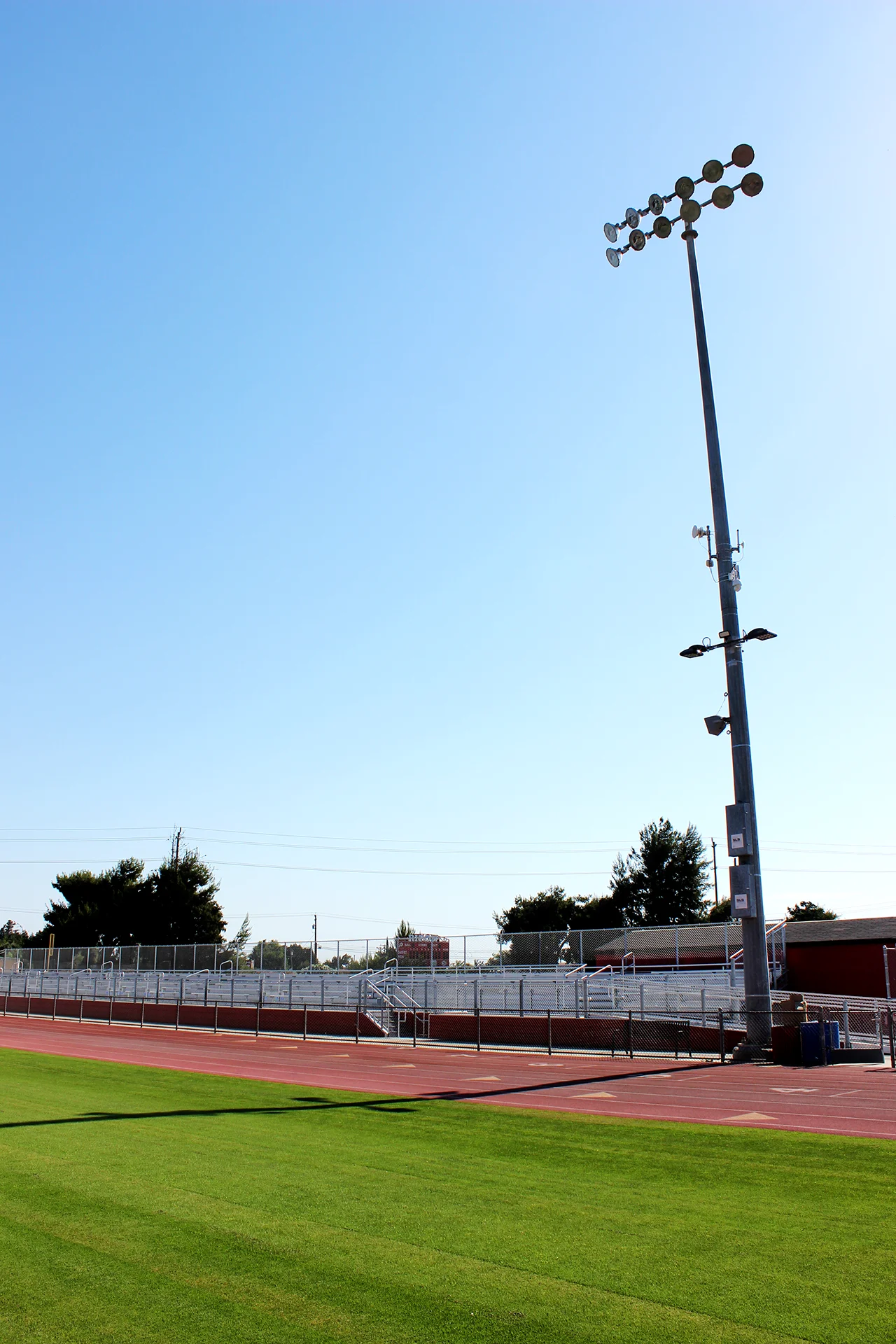 Tall stadium light pole overlooking Ripon High School’s running track, athletic field, and spectator bleachers on a clear day.