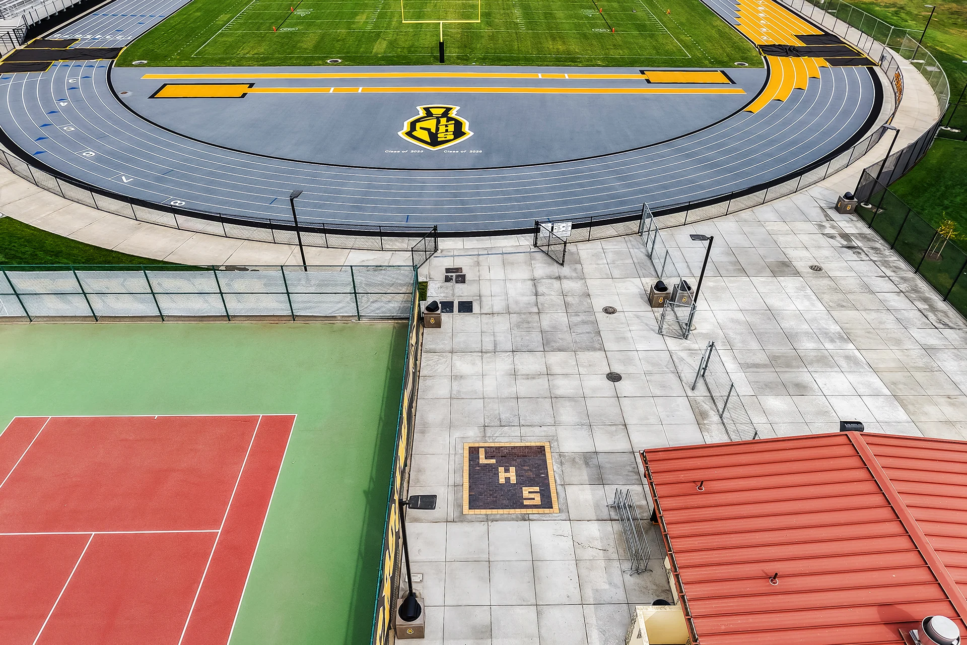 Elevated view of a grey and yellow synthetic running track curve next to concrete flatwork and a red-roofed field house.