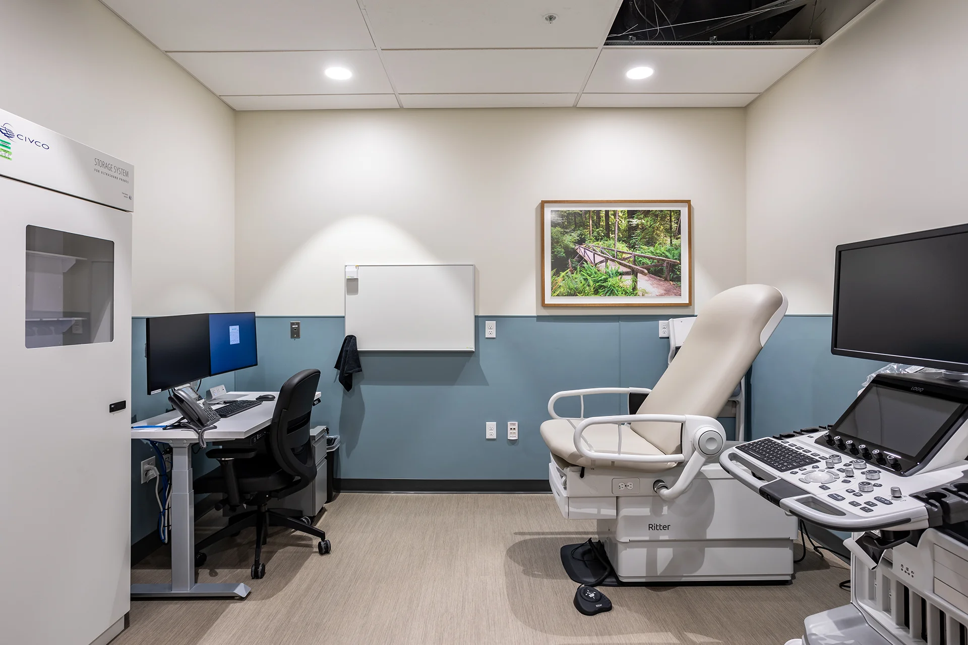 Medical imaging suite in Manteca, California, featuring a GE LOGIQ ultrasound machine, a white Ritter adjustable examination table, an Ergotron computer workstation, a wall-mounted whiteboard, and a CIVCO storage cabinet over light-colored resilient sheet vinyl flooring.