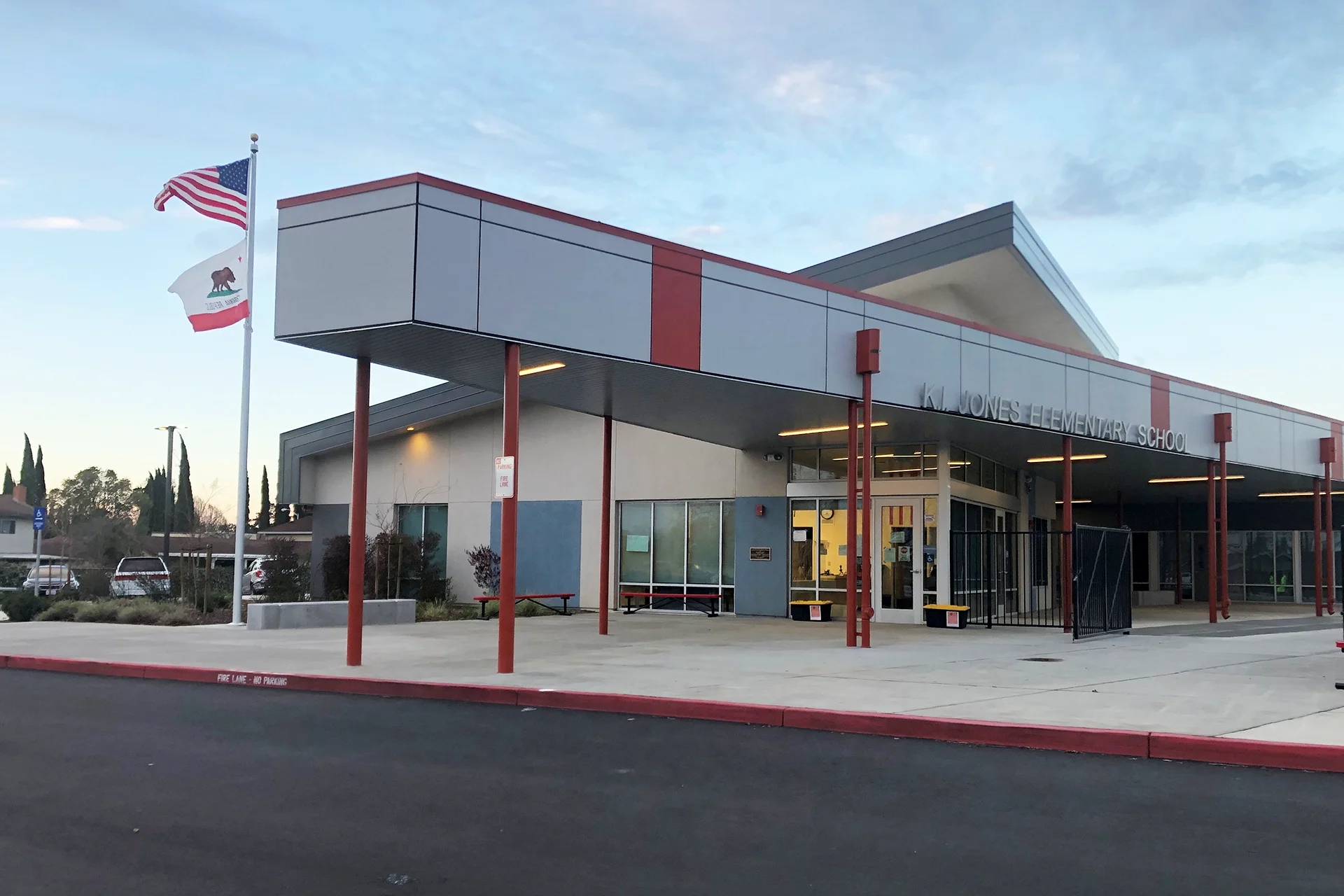 Front entrance plaza of K.I. Jones Elementary School featuring a covered student drop-off area, secure entry, modern architecture, and American and California state flags.