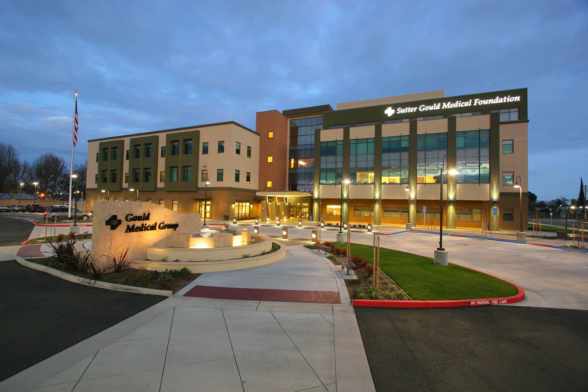 Twilight exterior of the Sutter Gould Medical Foundation medical office at 600 Coffee Road featuring the illuminated healthcare building, monument sign, landscaped entrance, and welcoming patient arrival plaza.