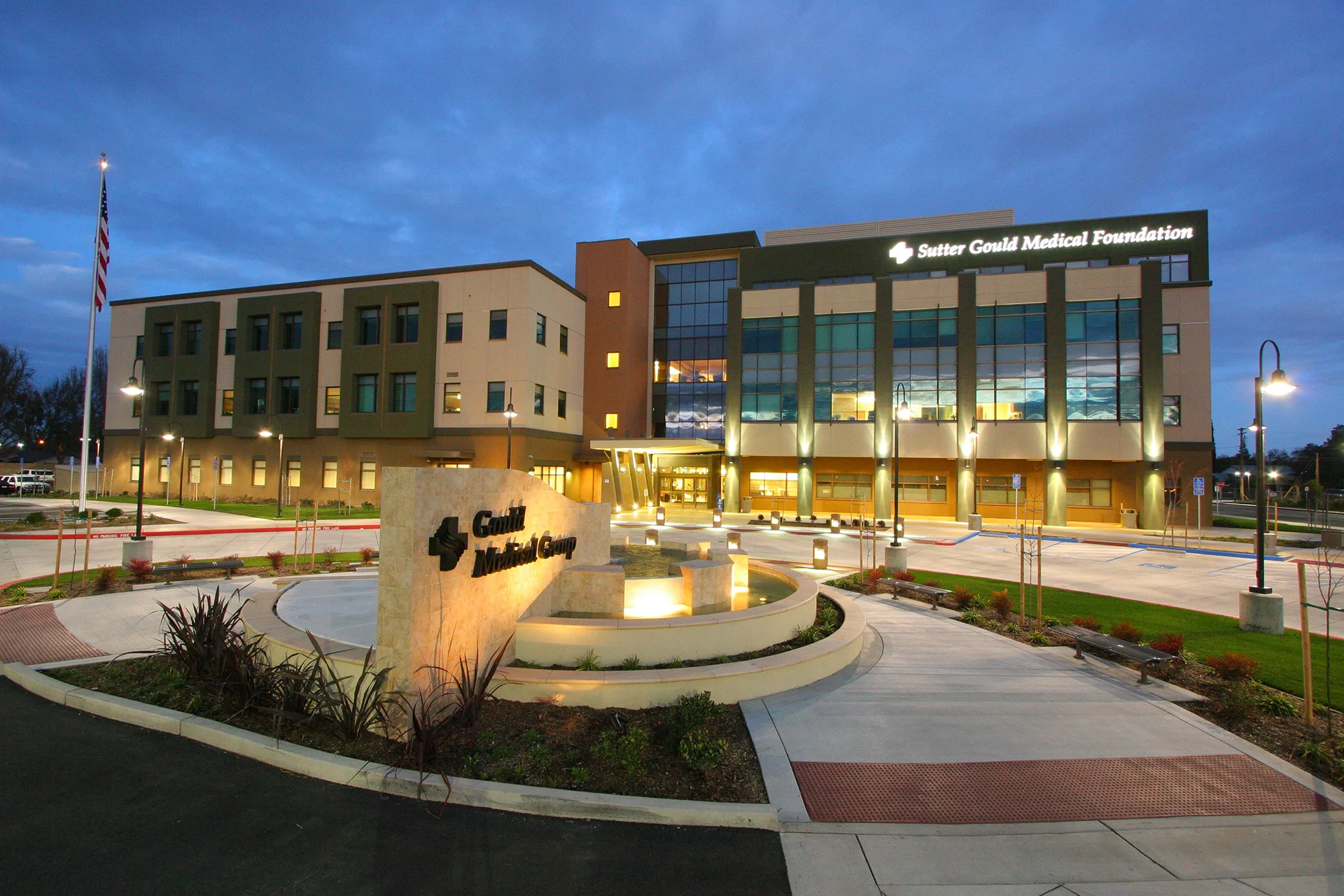Evening view of the Sutter Gould Medical Foundation healthcare campus at 600 Coffee Road featuring the illuminated medical office building, monument sign with water feature, landscaped entrance, and accessible patient pathways.