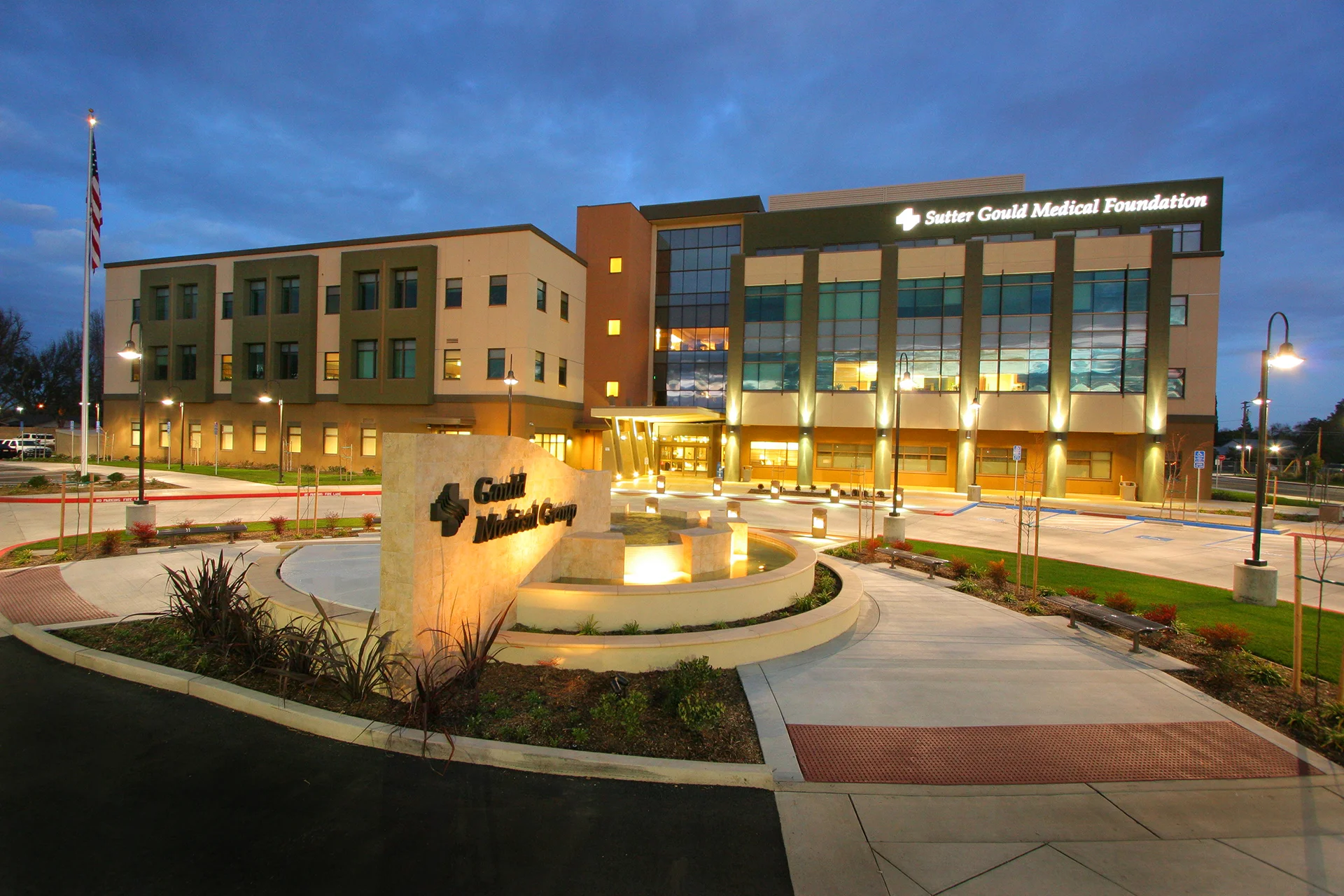 Exterior view of the Sutter Gould Medical Foundation medical office at 600 Coffee Road featuring a modern healthcare facility, illuminated entrance, landscaped plaza, and patient drop-off area at dusk.