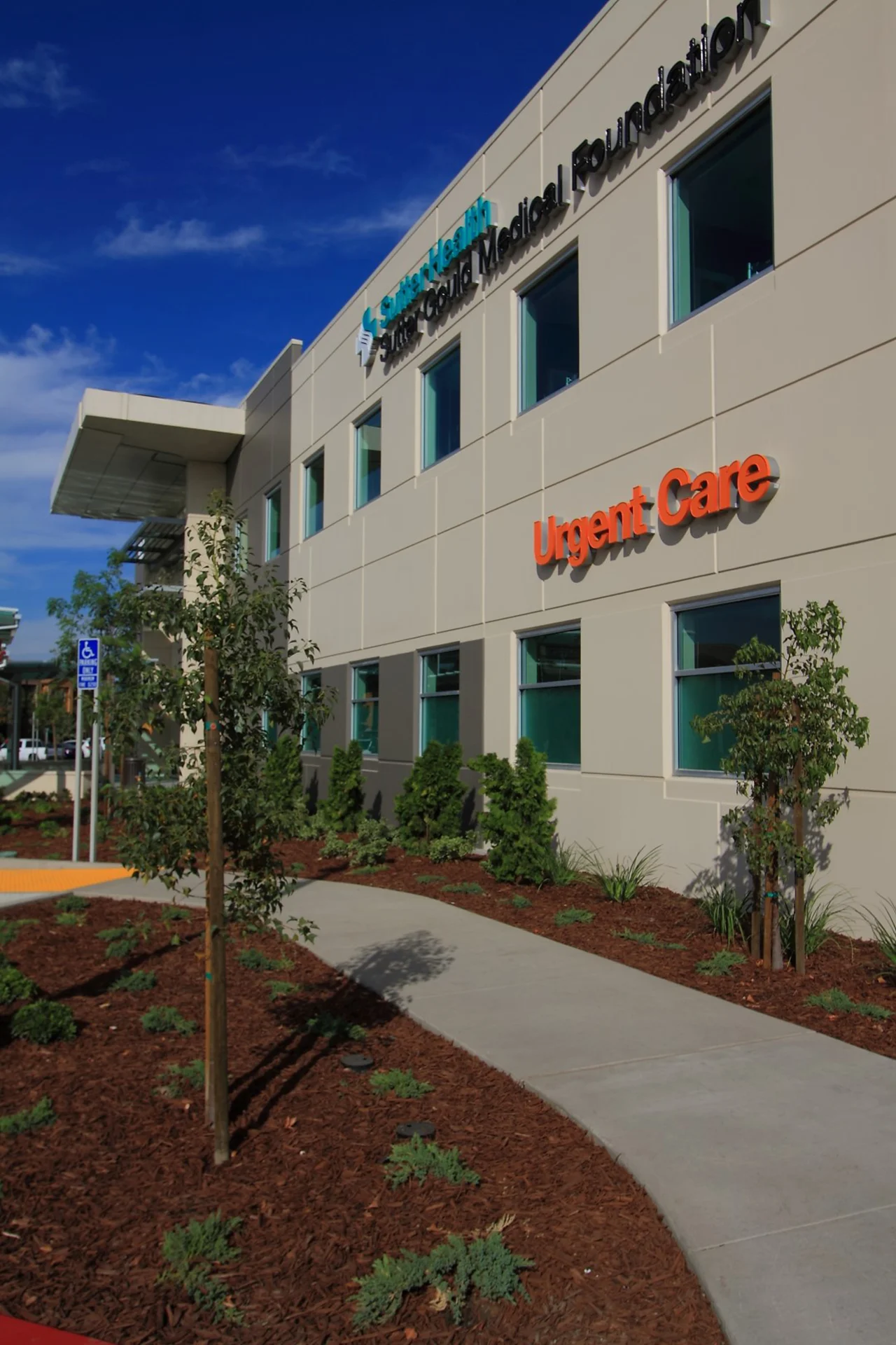 Exterior of the Sutter Gould Turlock Medical Office Building featuring the Urgent Care entrance, landscaped pedestrian walkway, accessible access, and contemporary healthcare facility design.
